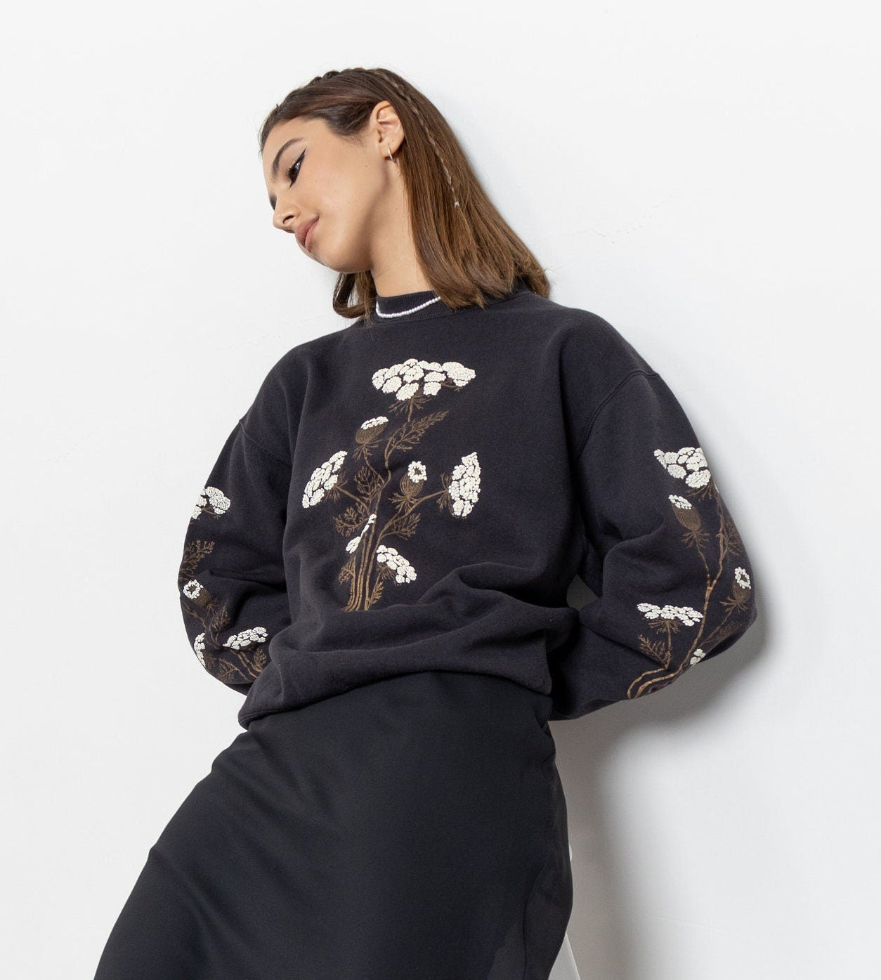 Woman wearing a black floral embroidered top and black skirt with black shoes on a white background