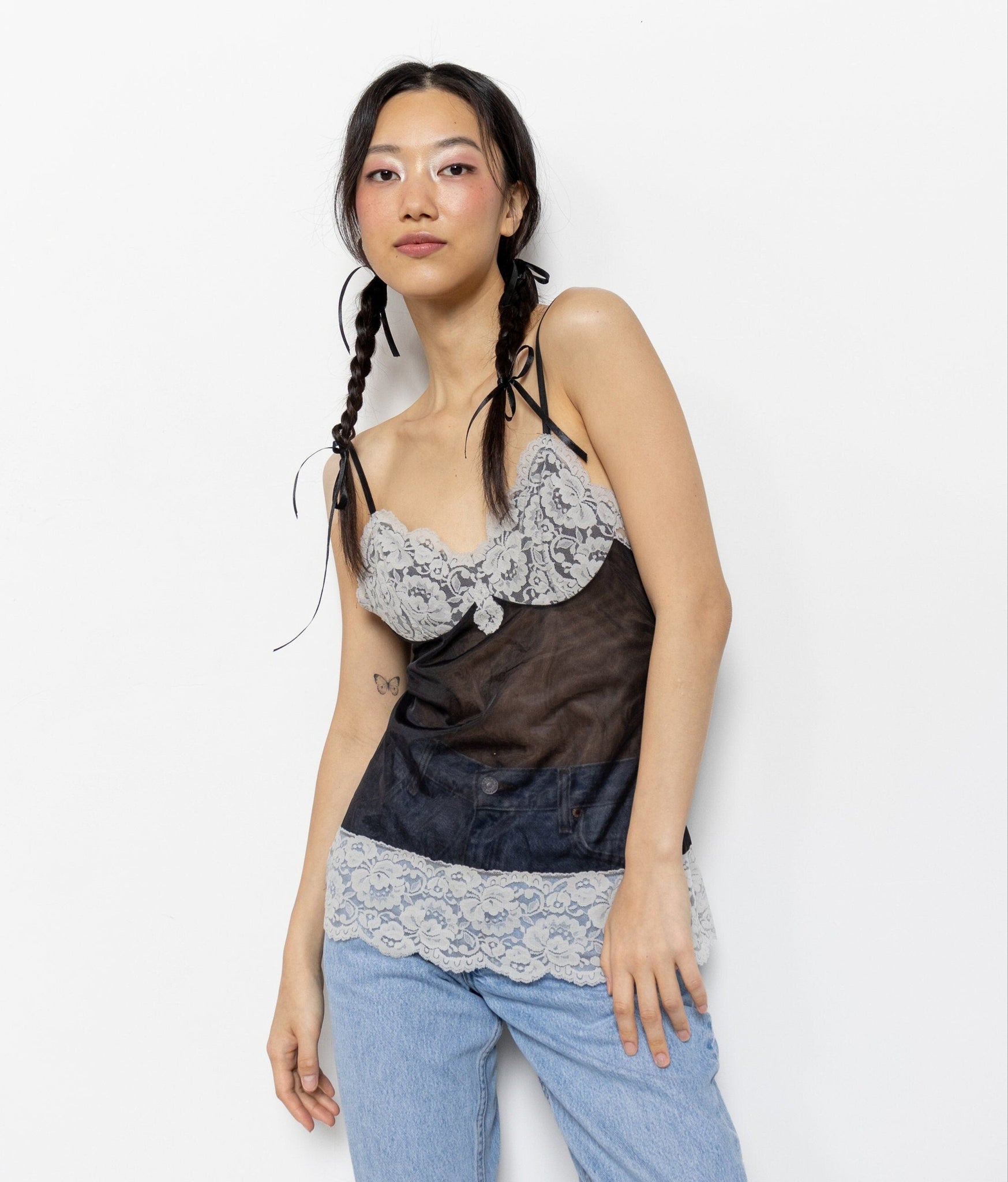 A model wearing a vintage 80's sleeveless black mesh camisole with white lace trim and bustline, paired with blue jeans.