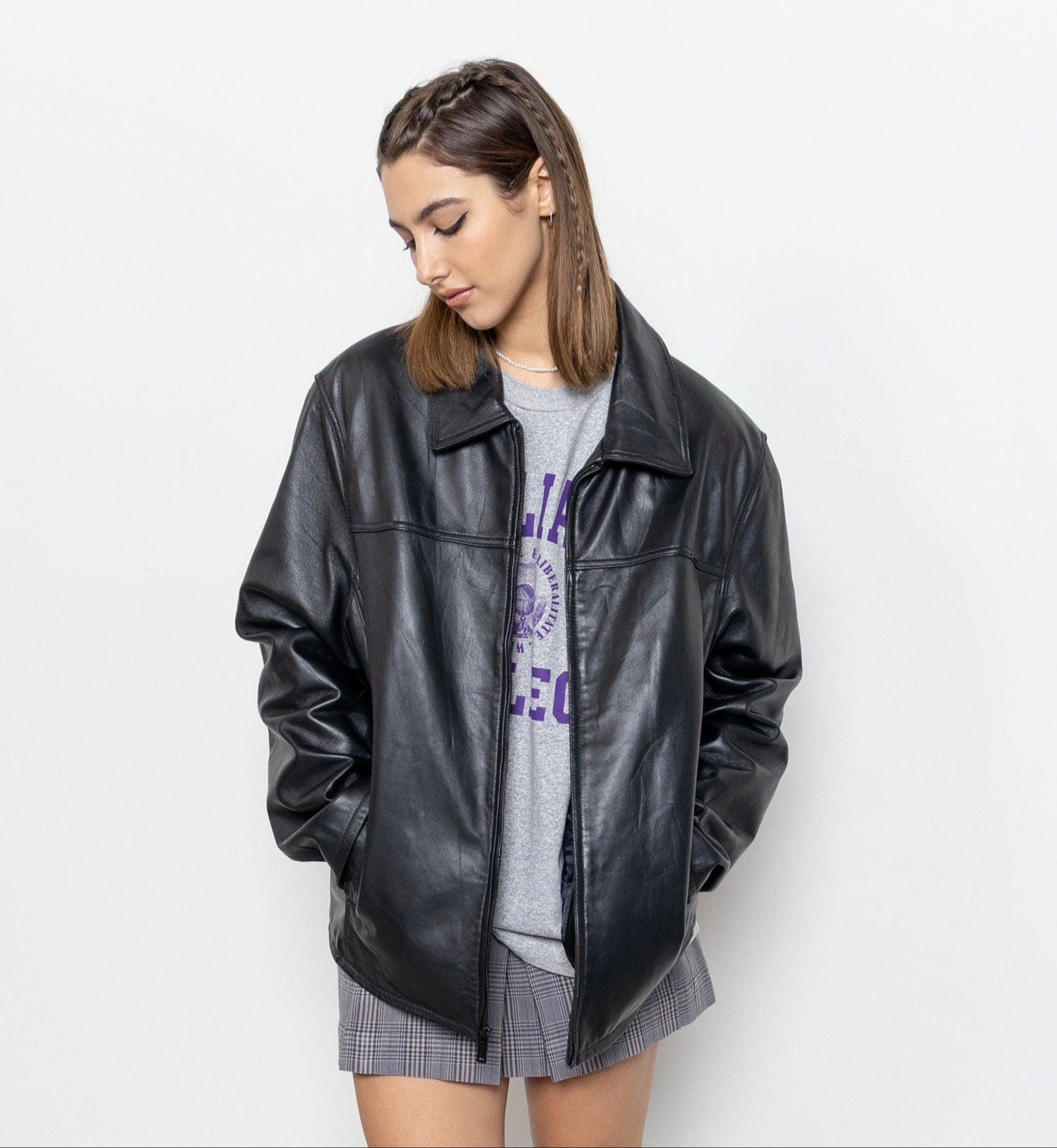 Person wearing a black leather jacket over a graphic t-shirt with a plain background