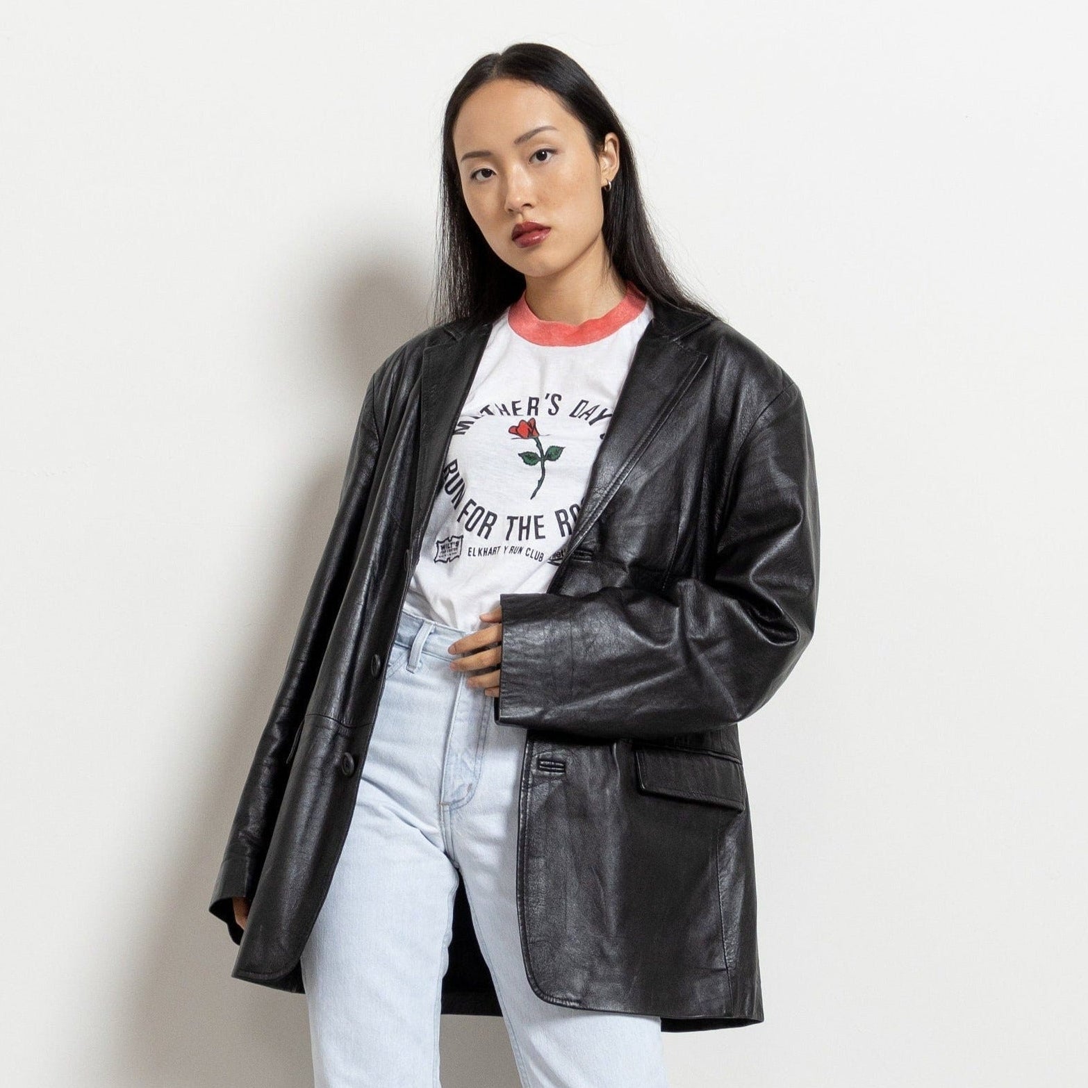 Person wearing a black leather jacket over a graphic t-shirt on a plain background