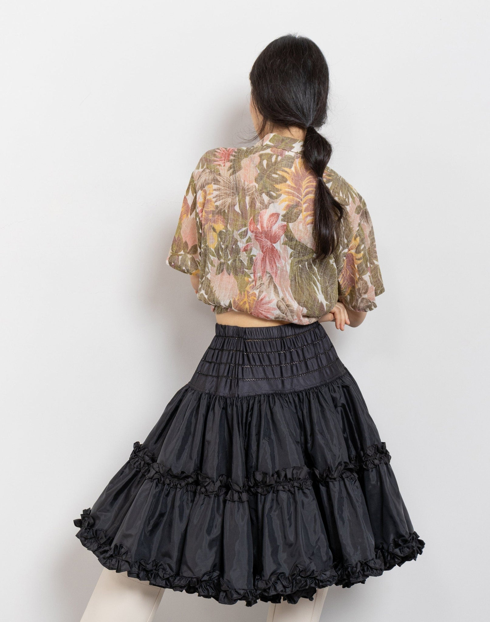 Person wearing a floral blouse and black ruffled skirt on a white background