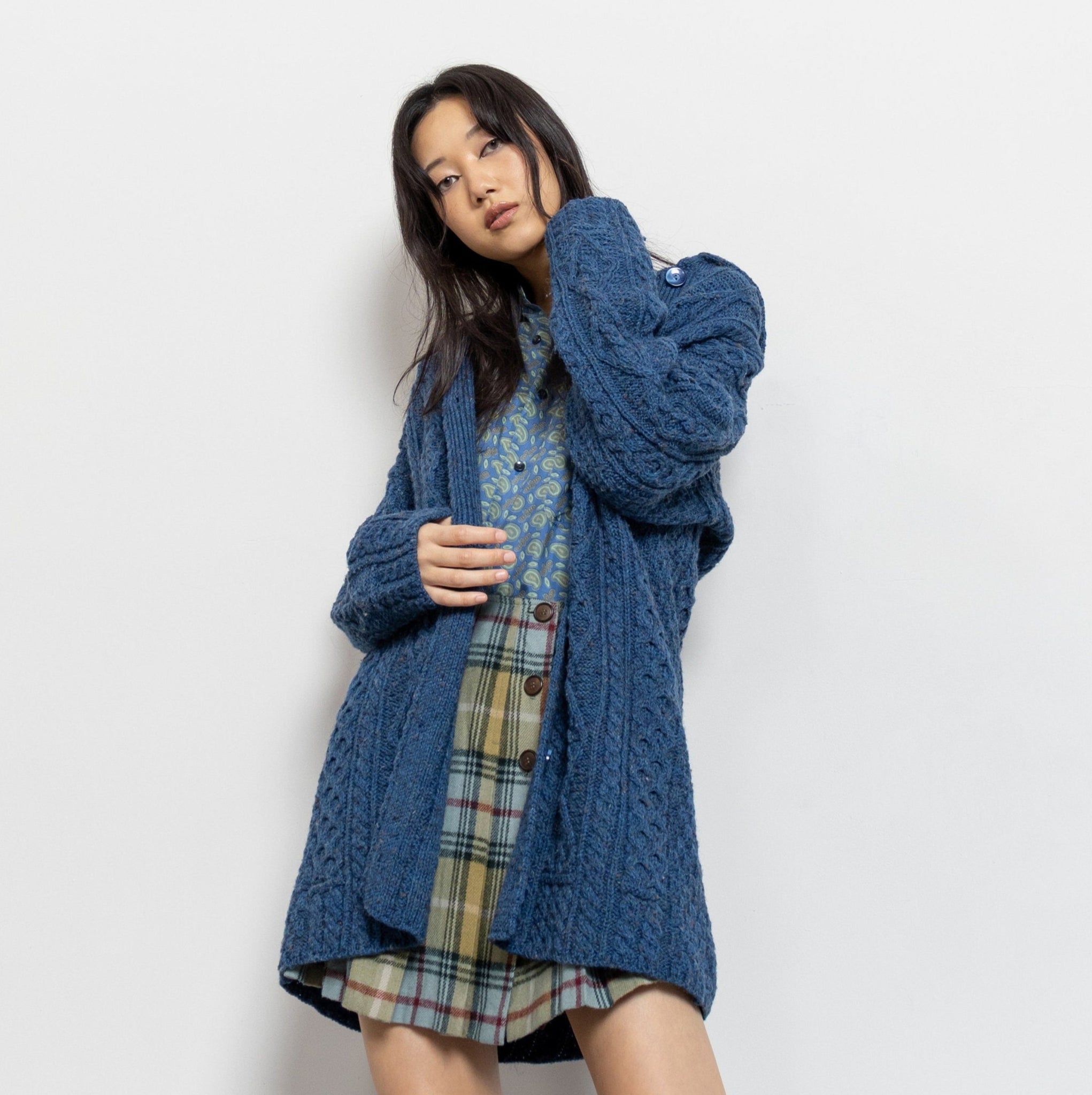 Woman wearing a blue knitted cardigan over a plaid dress on a white background