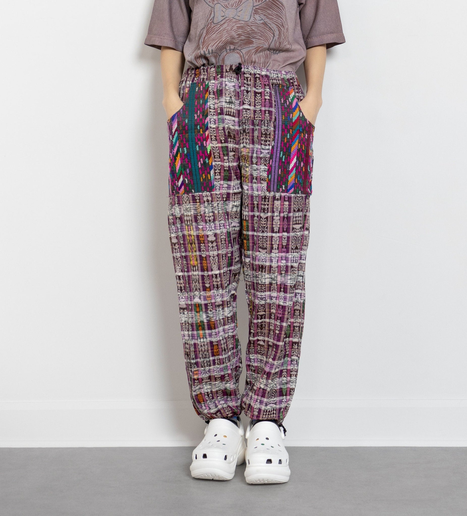 A person standing wearing high-waisted, woven cotton pants with colorful geometric patterns and drawstrings. 
