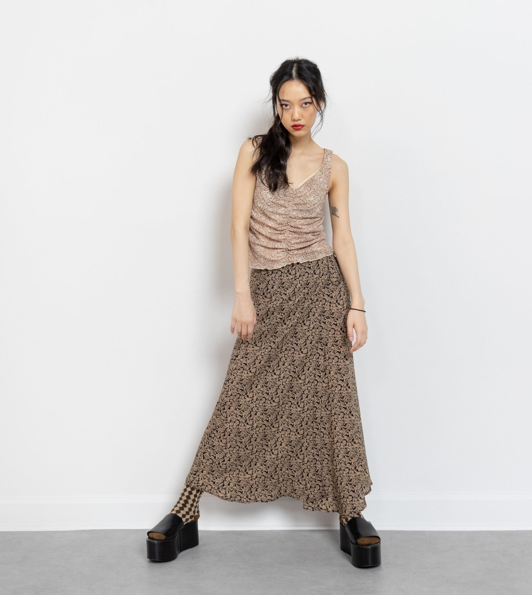 A person standing wearing an ankle-length floral maxi skirt with a tie at the waist, in muted brown and black tones.