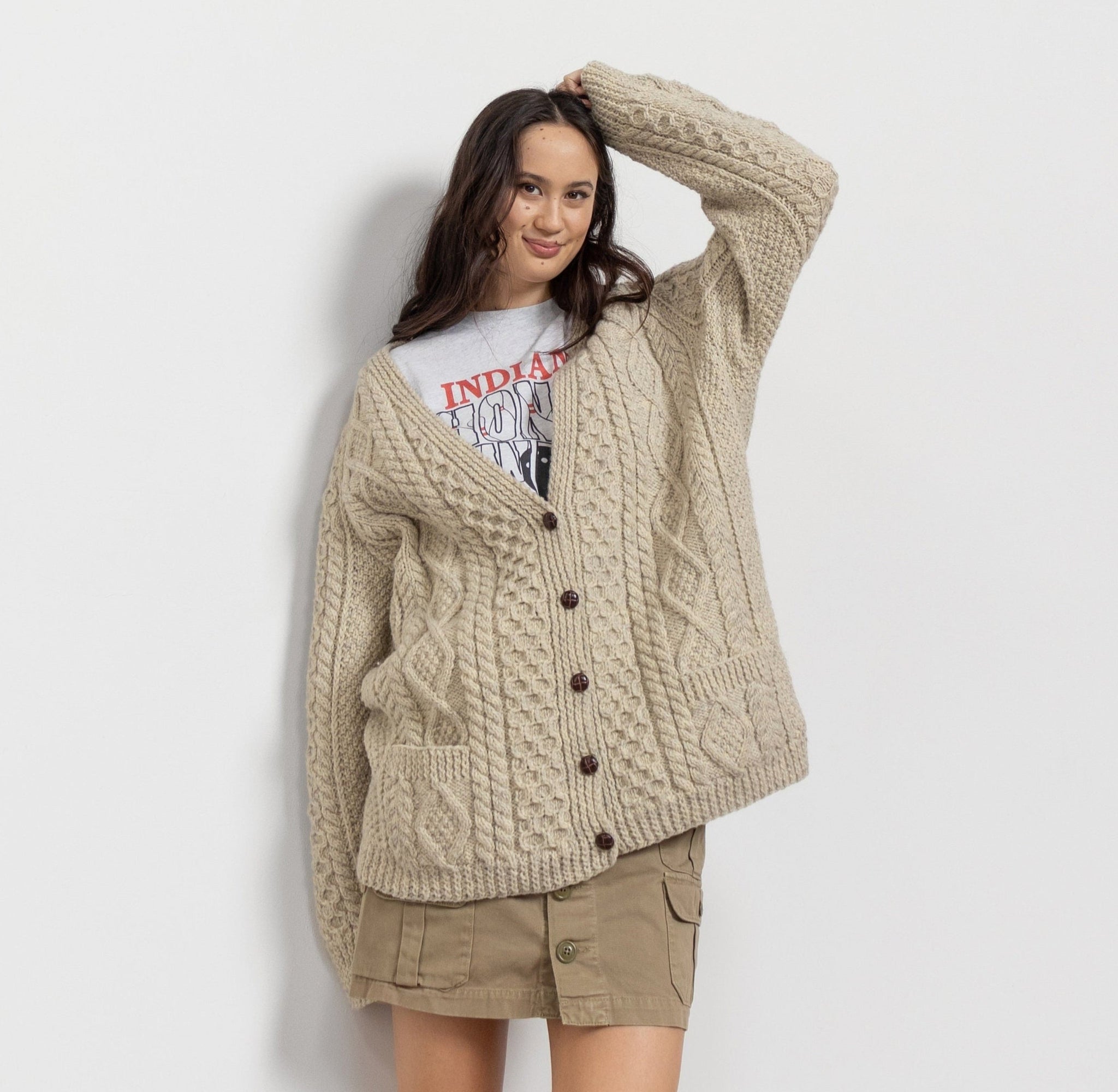 A woman smiling and posing in a beige cable knit Irish wool cardigan with buttons and two front pockets.
