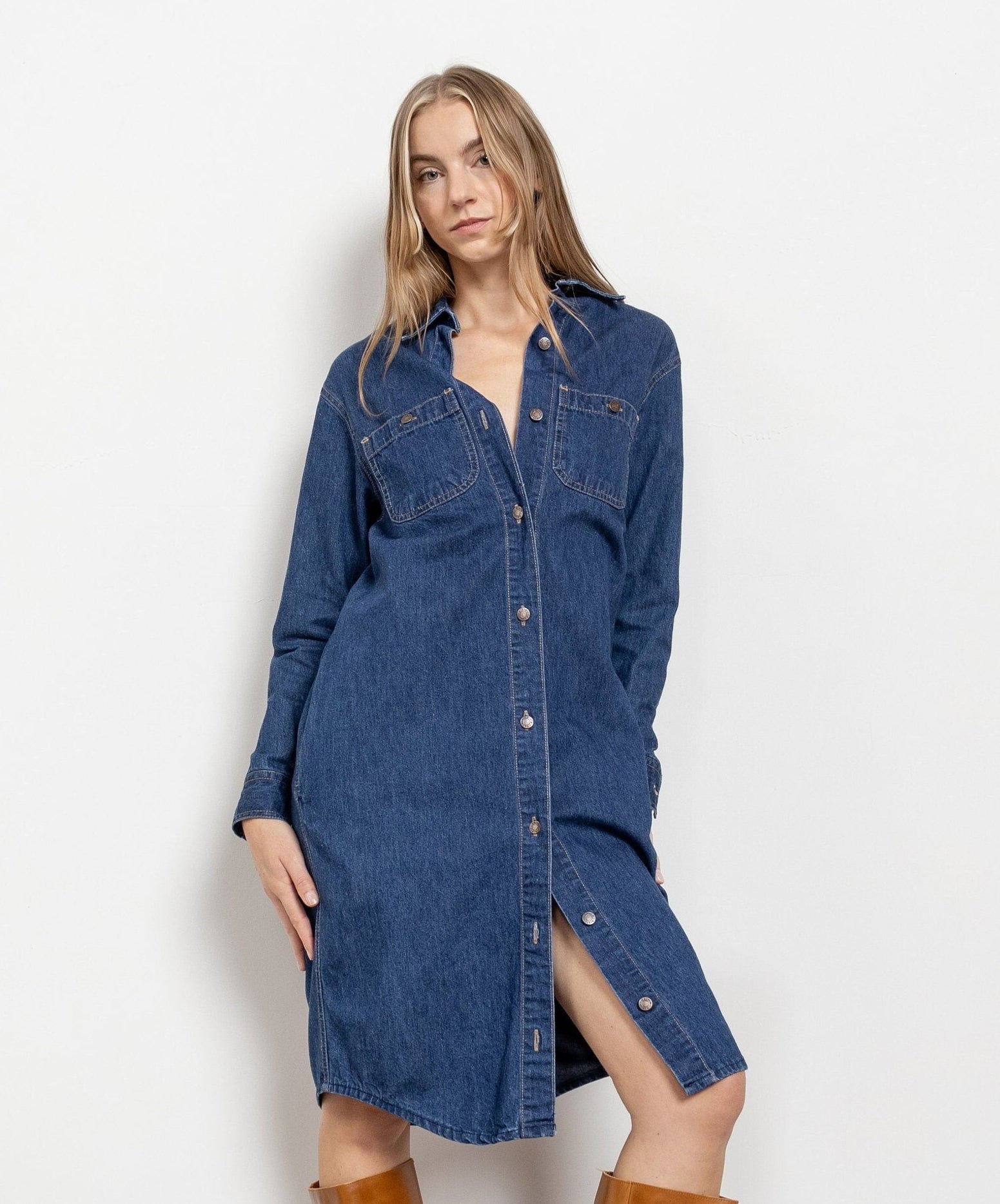 A woman modeling a vintage long sleeve denim midi dress with buttons down the front, two side pockets, and a collar.