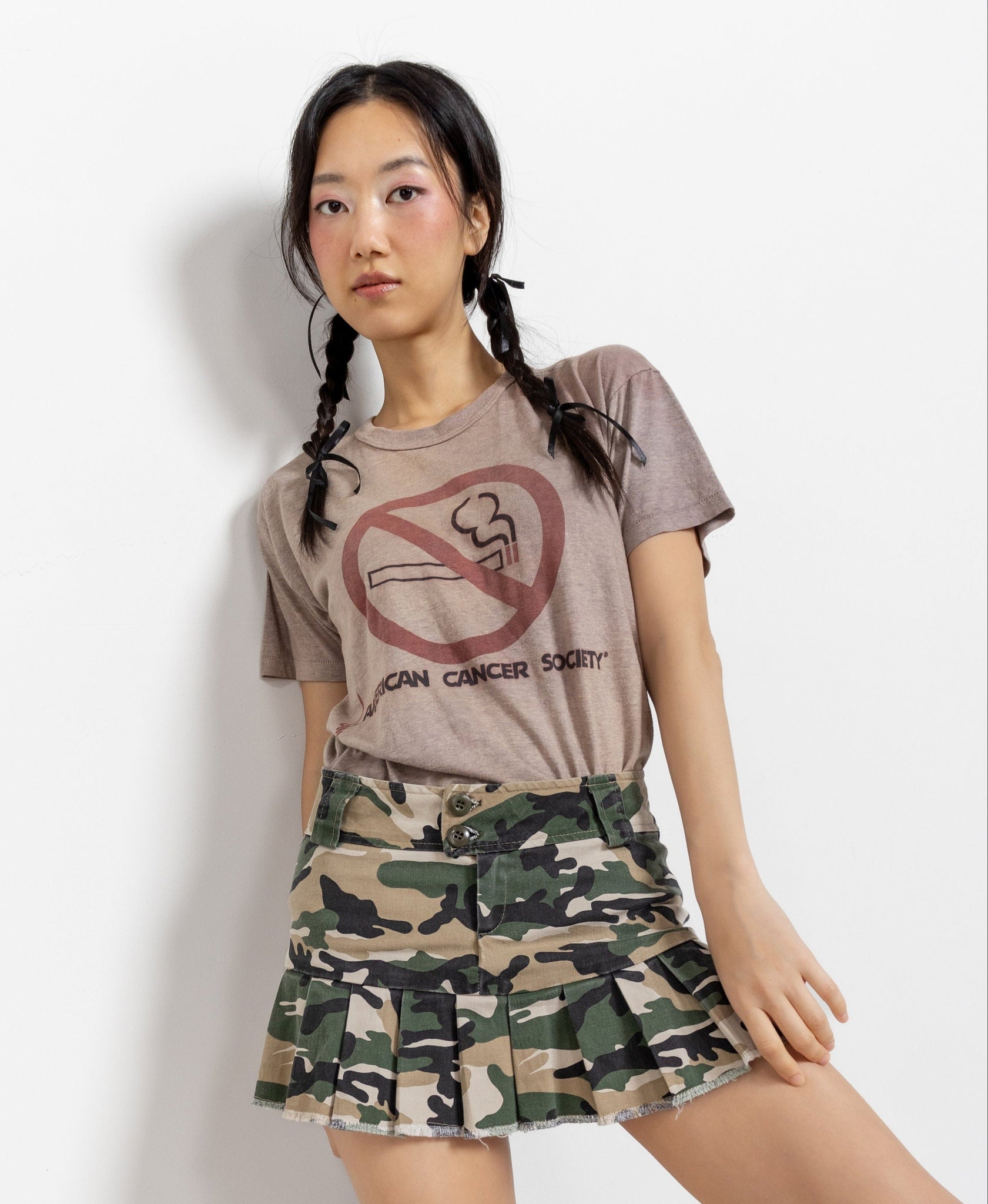 Person wearing a t-shirt with a no smoking graphic and camouflage skirt on a white background