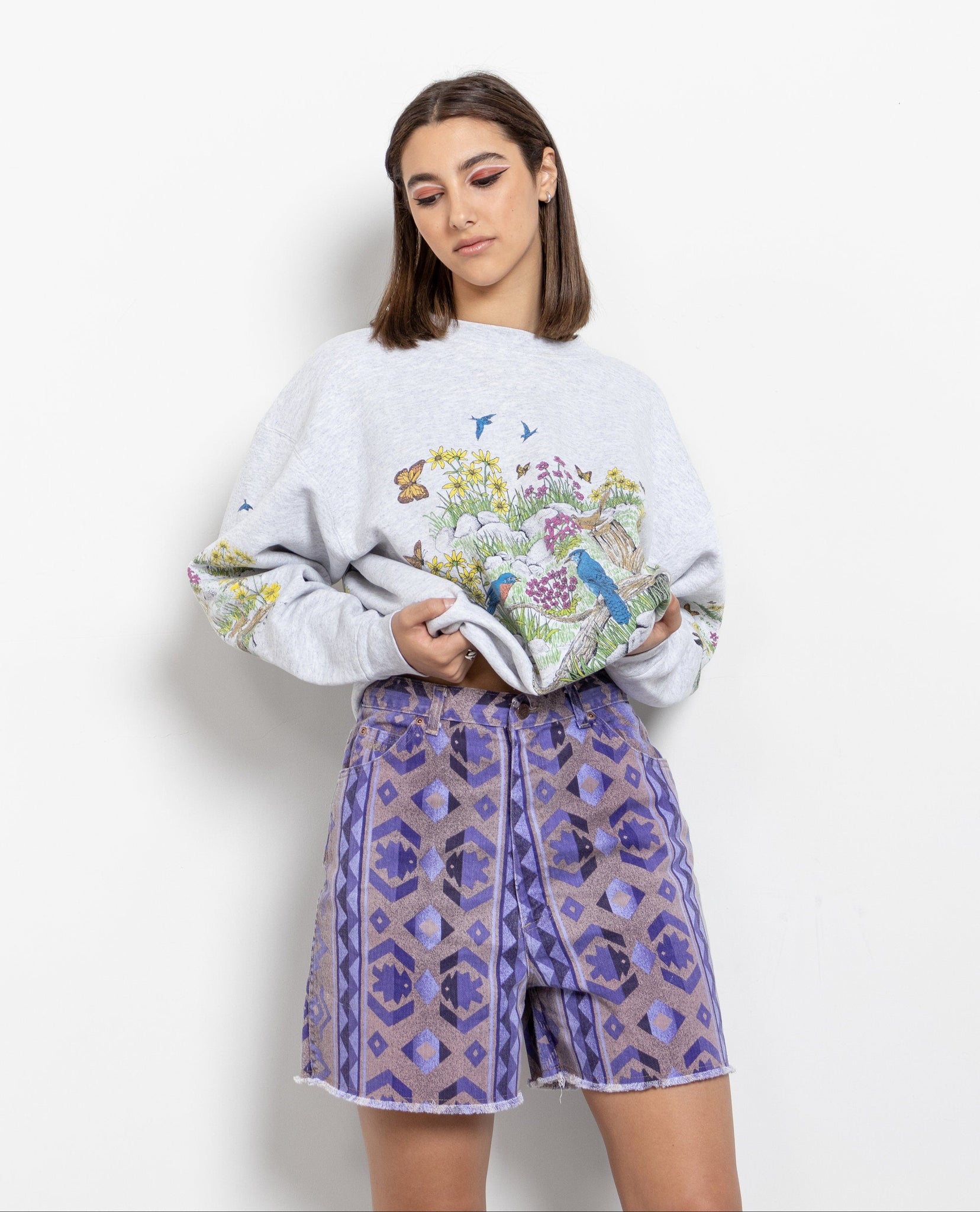 A person wearing a white vintage-style shorts with a geometric pattern and a longer length, paired with a graphic t-shirt.