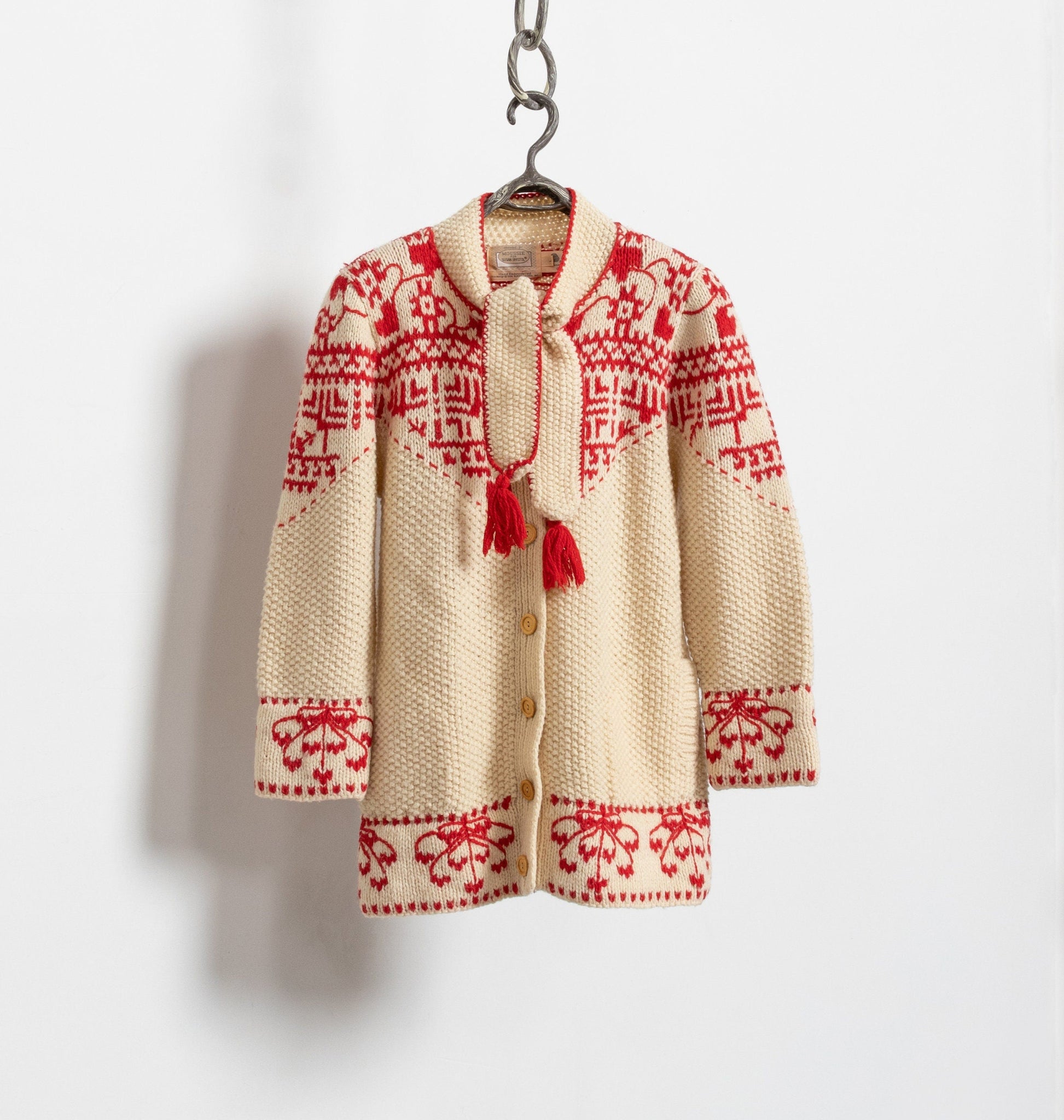A vintage 90's hand knit cardigan with red embroidery and oversized wooden buttons, displayed on a hanger against a white background.