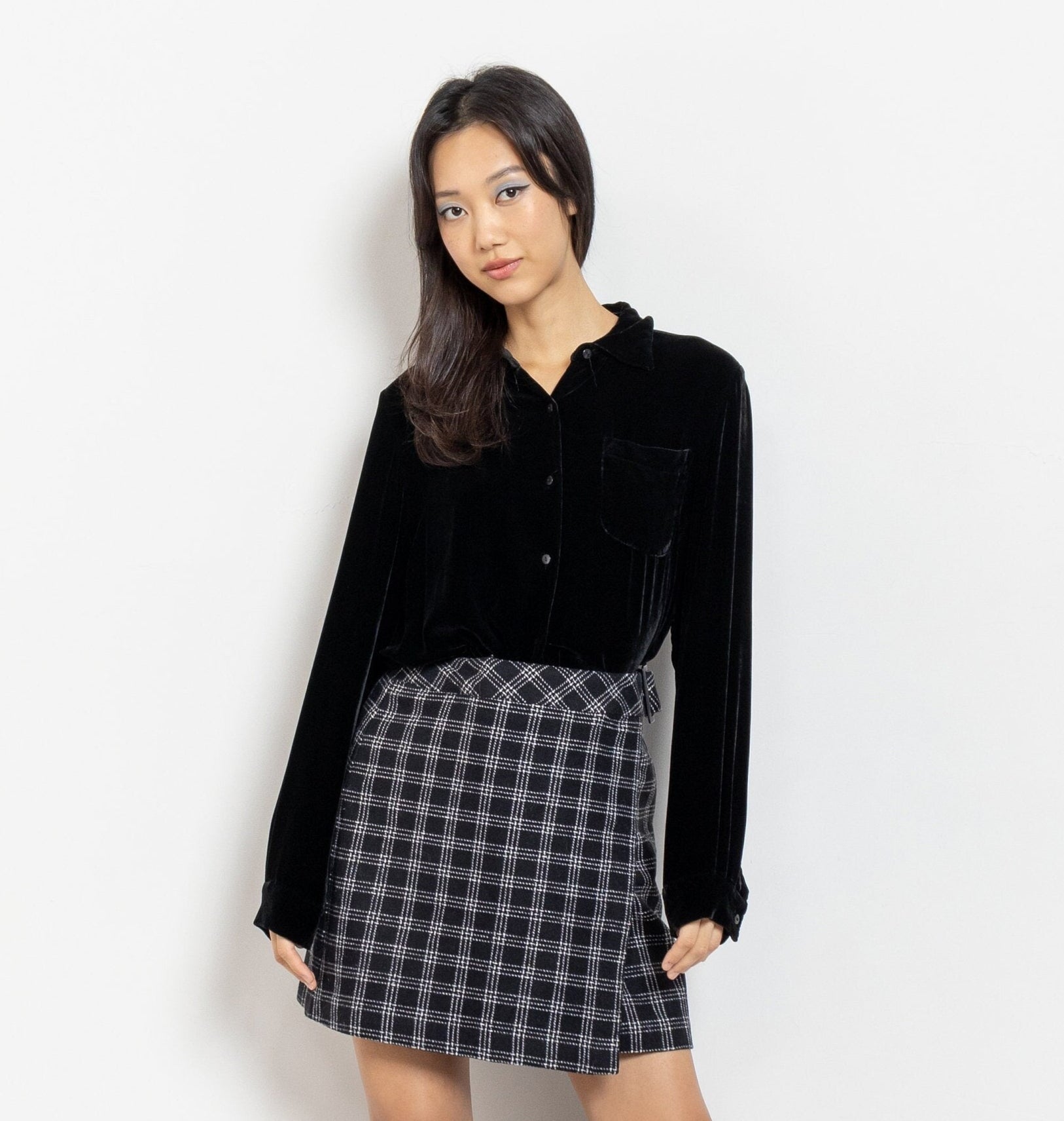 Woman wearing a black shirt and plaid skirt against a white background