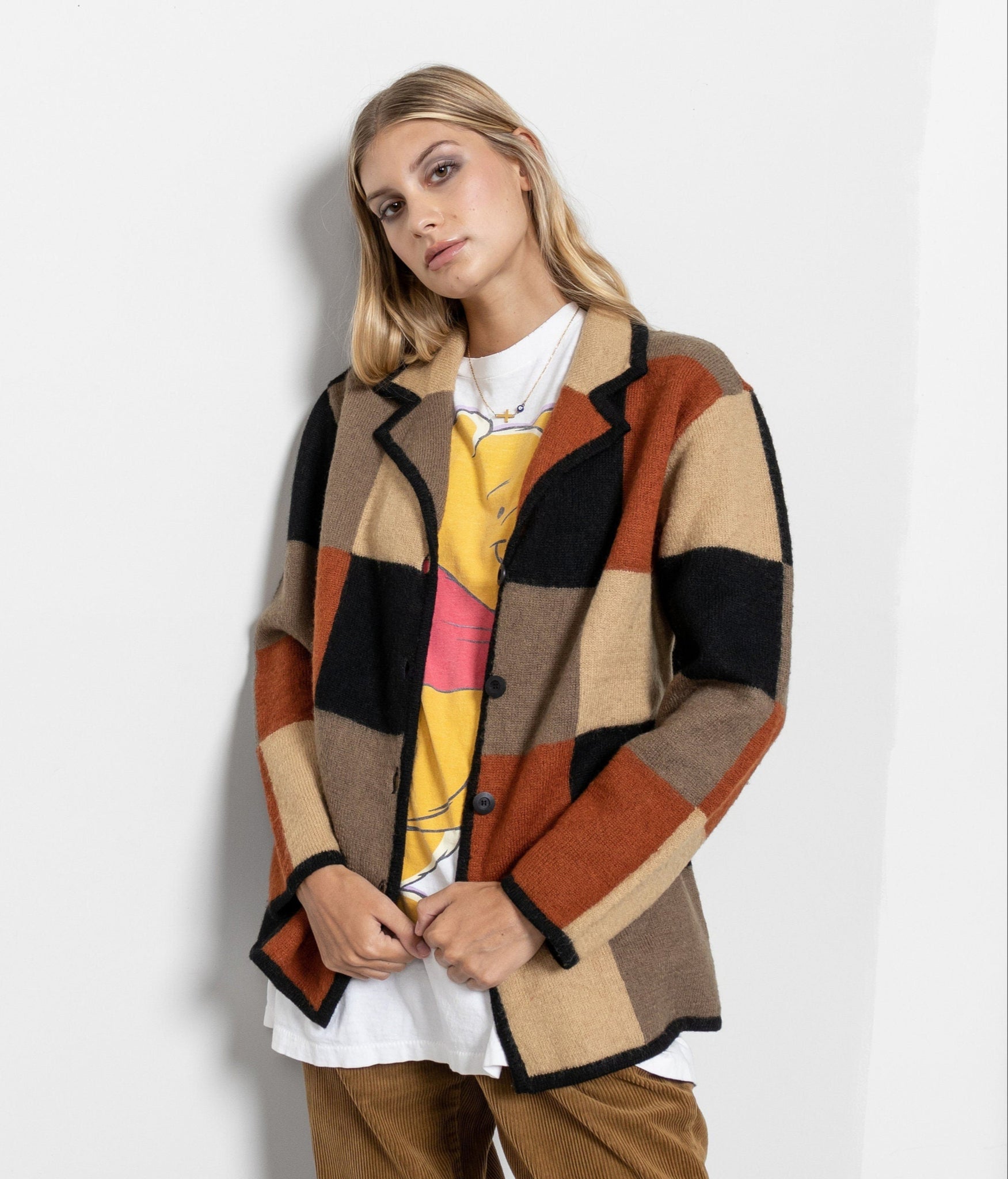 A woman wearing a checkered wool sweater in brown and orange tones with a notched collar and buttons down the front, paired with brown trousers.