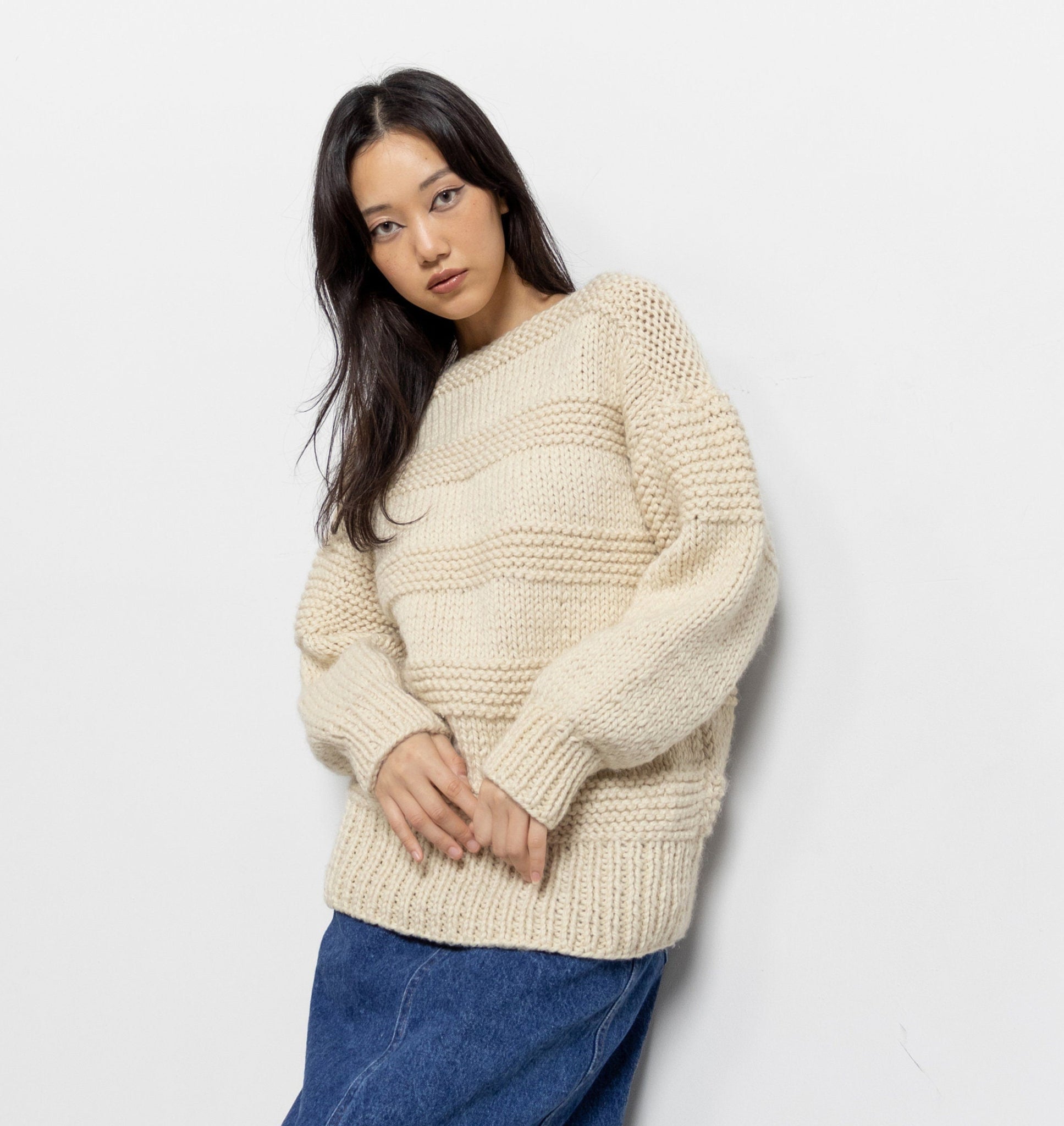 Woman wearing a cream sweater and blue jeans against a white background