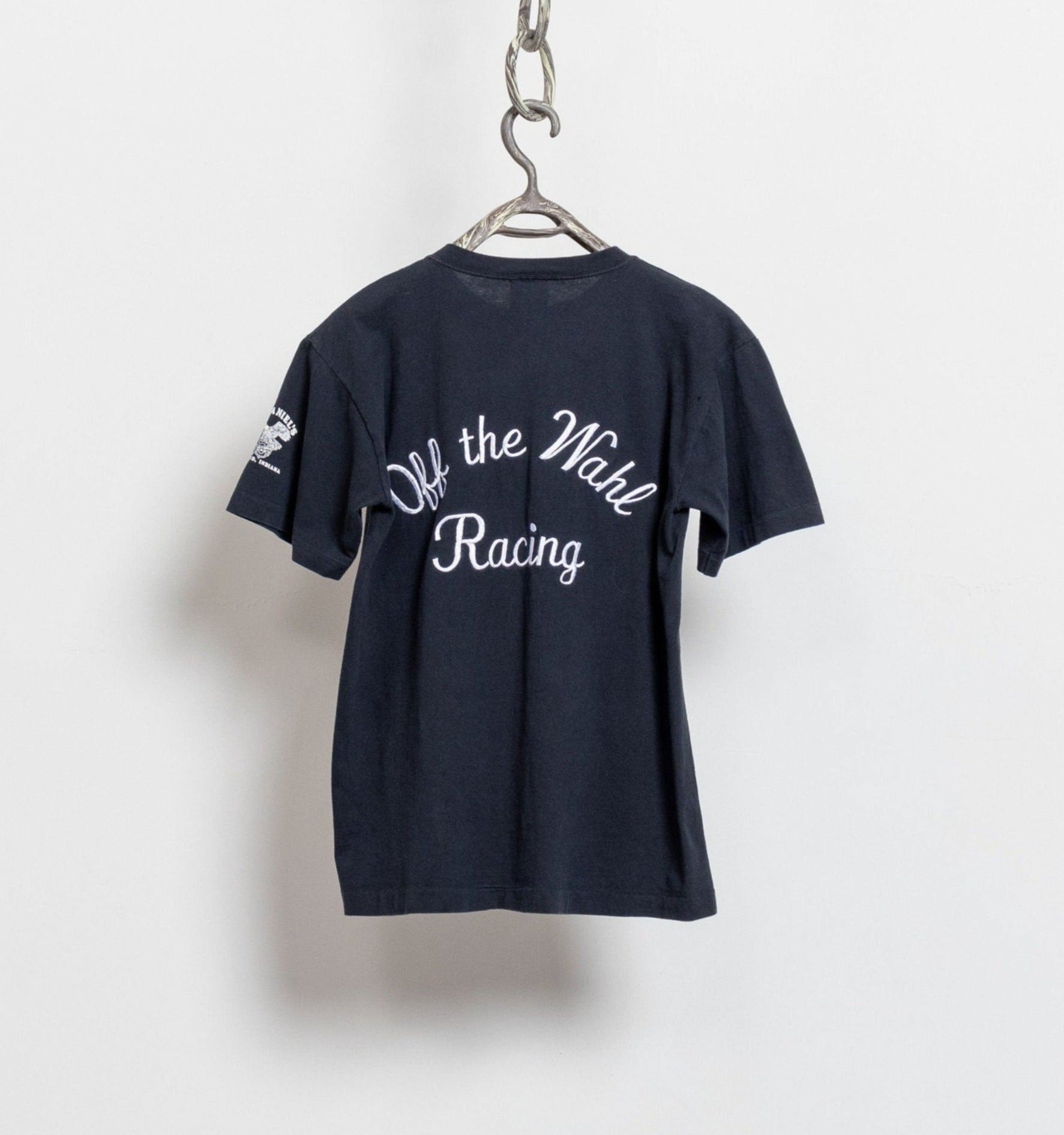 A navy blue Harley Davidson Motorcycles short sleeve t-shirt with orange and white text embroidery, hanging on a display hanger.