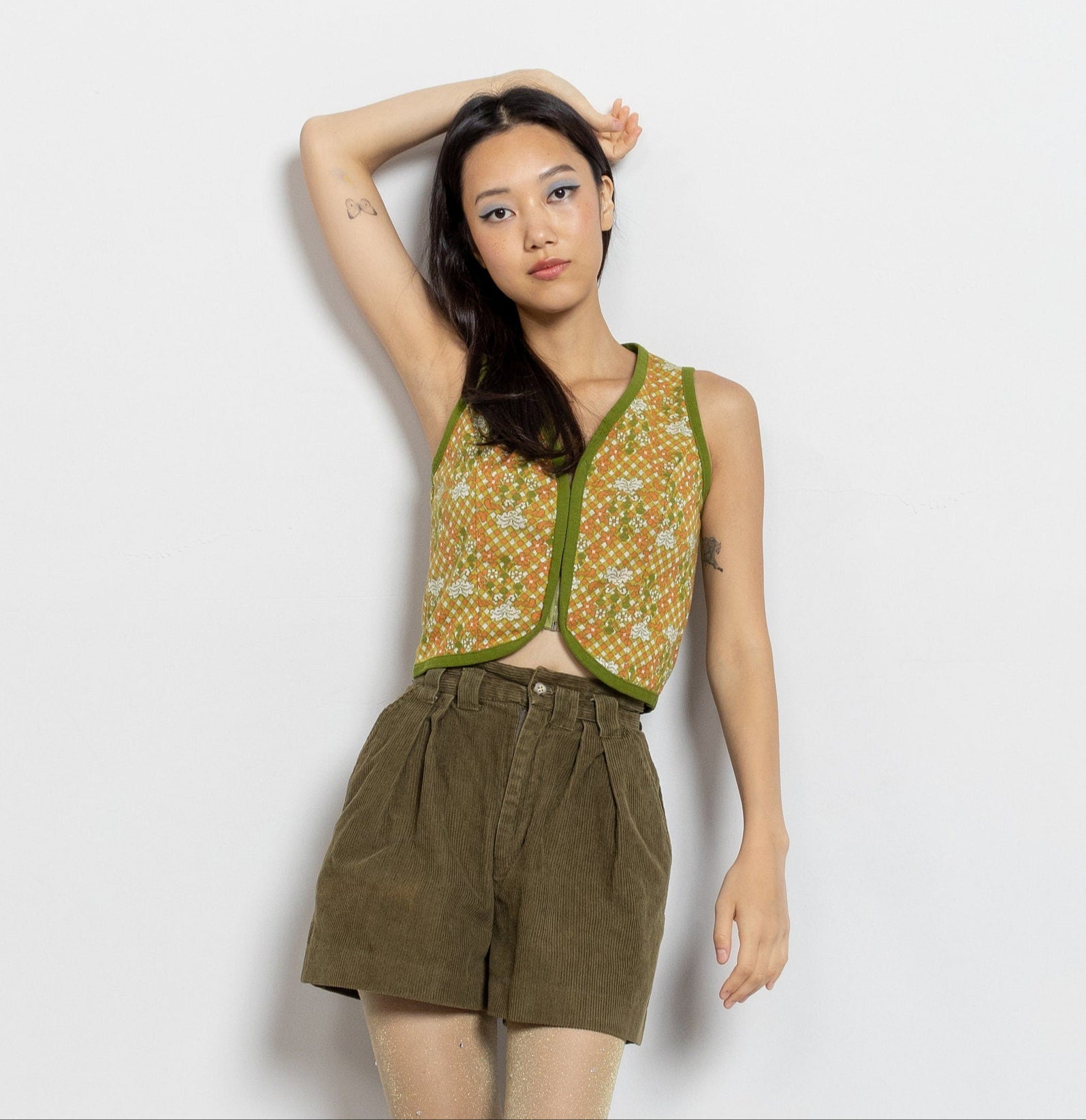 Woman wearing a green sleeveless top and brown shorts with orange boots on a white background