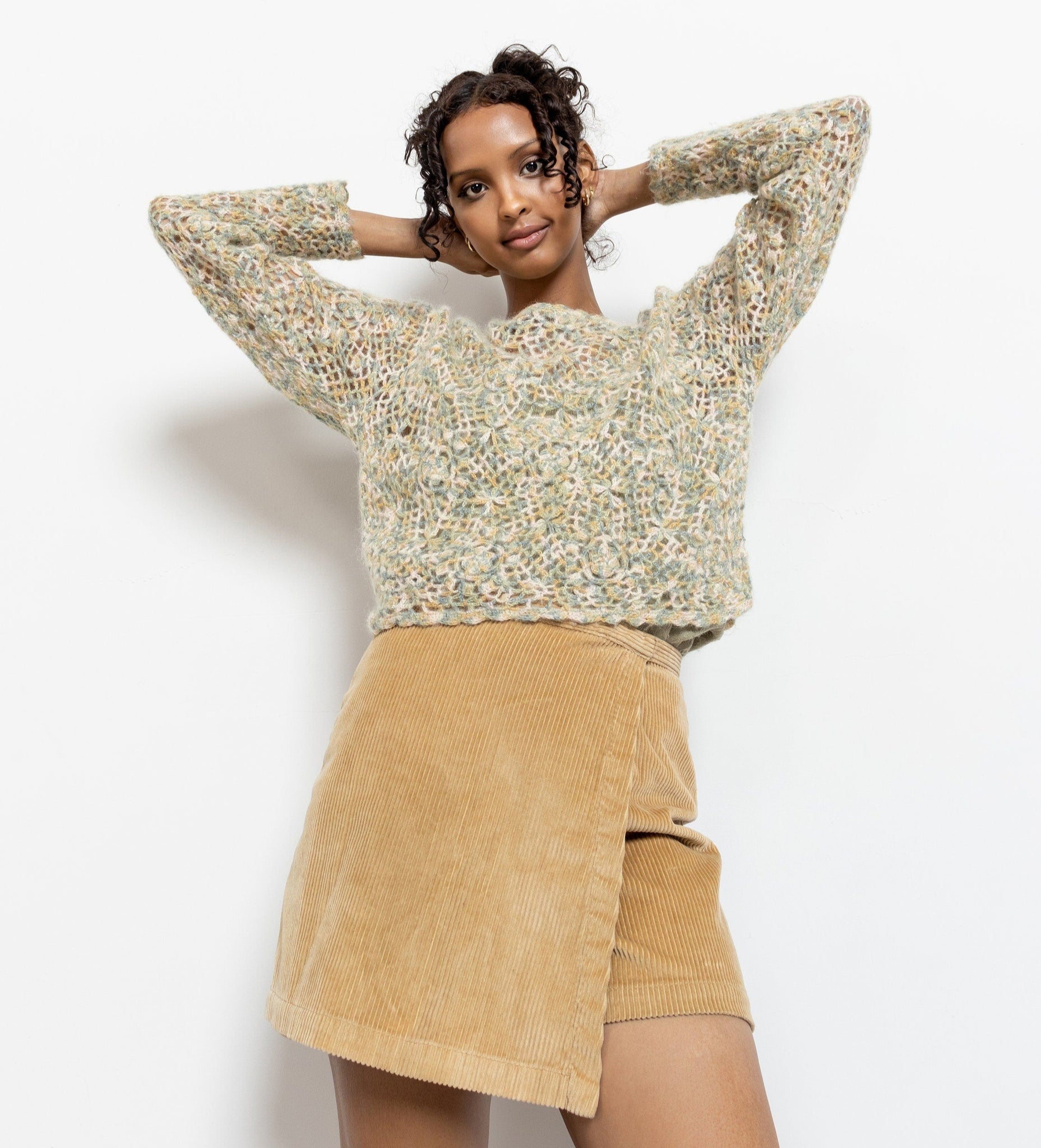 Woman wearing a textured sweater and beige skirt on a white background