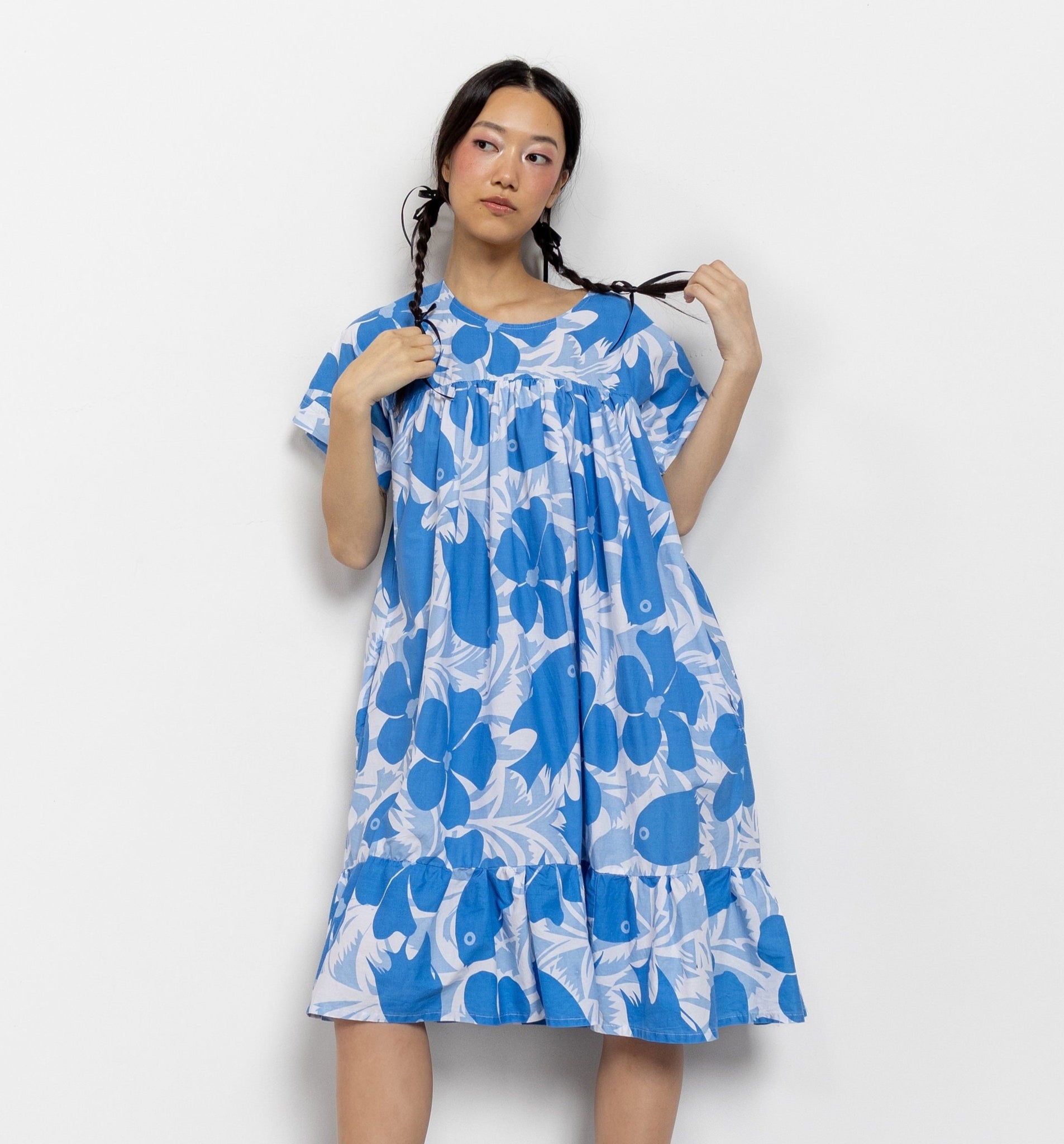 A person wearing a blue floral print cotton sleeping dress with short sleeves and a ruffled bottom, posing against a white background.