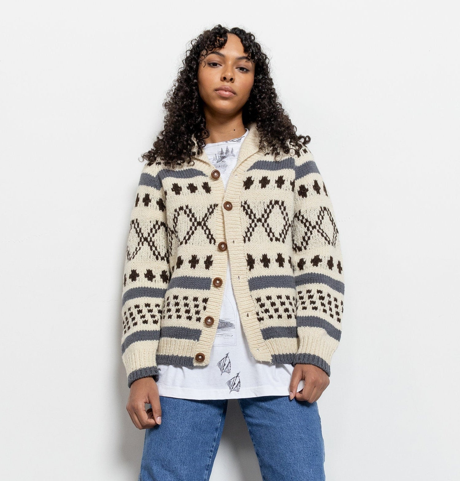 Person wearing a patterned cardigan, white shirt, blue jeans, and white sneakers on a white background