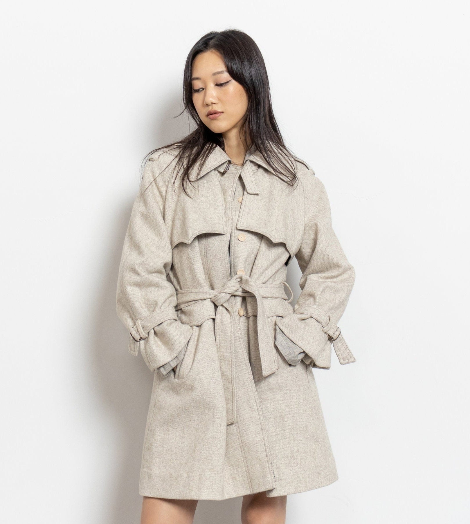 Woman wearing a beige trench coat against a white background