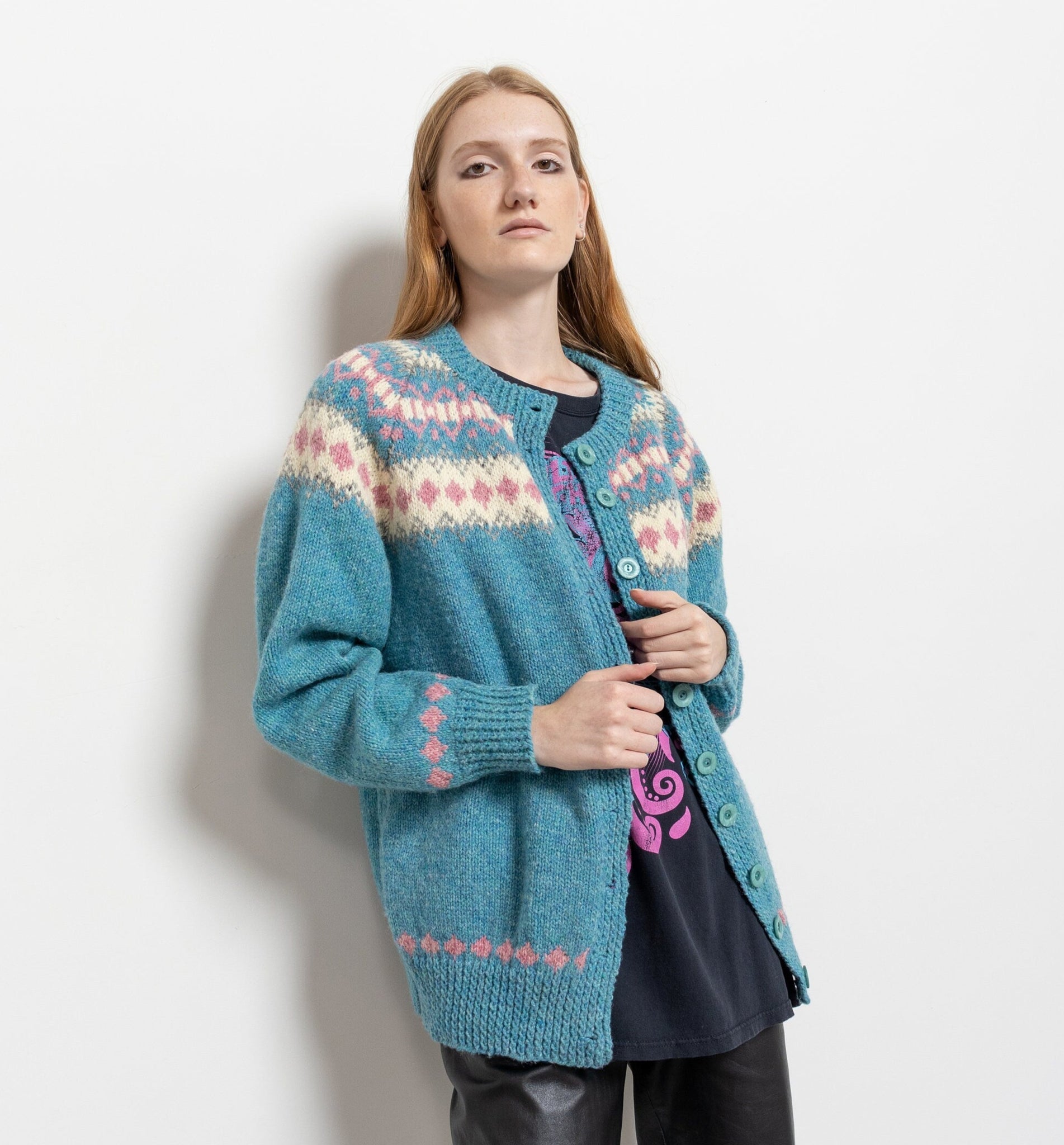 A woman wearing a vintage 90's traditional button-up fair isle wool cardigan in blue with pink and beige patterns.