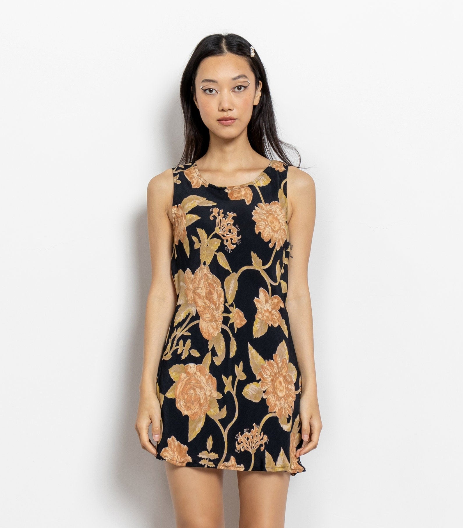 A sleeveless mini dress with a black background featuring a vintage floral pattern in shades of beige, brown, orange, and cream.