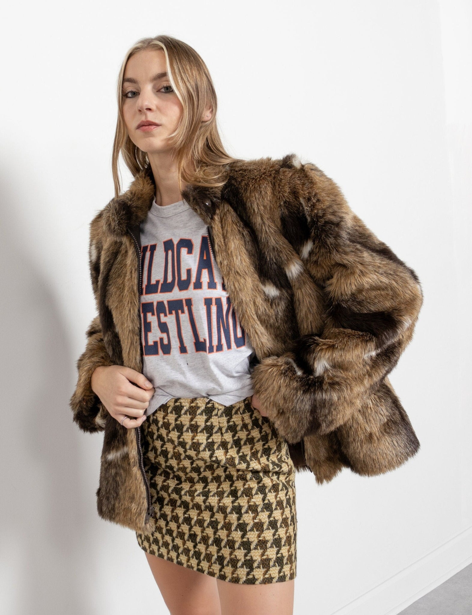 Woman wearing a fur coat, graphic t-shirt, and houndstooth skirt on a white background