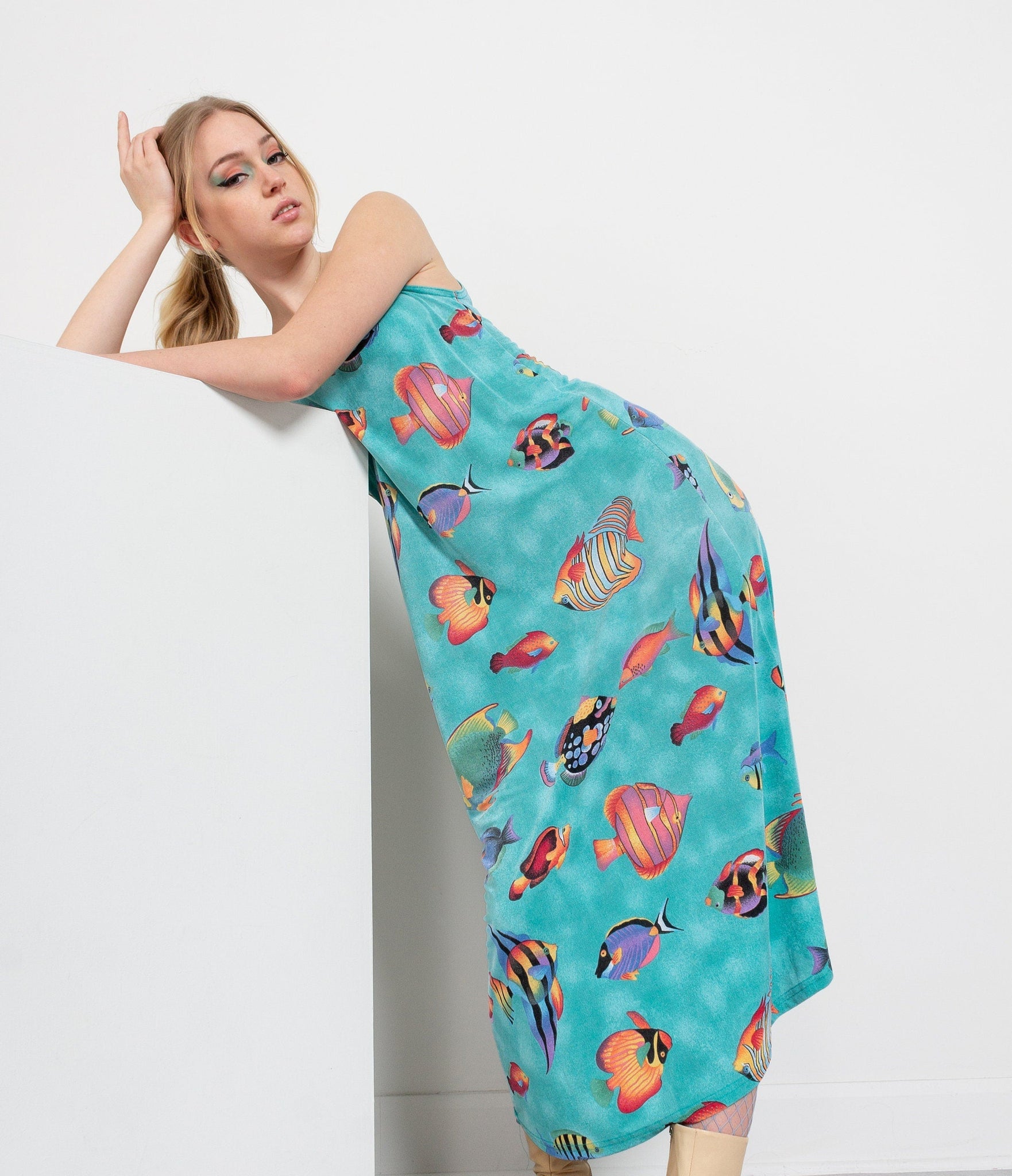 A person wearing a sleeveless midi dress with a tropical fish pattern on an aqua background.