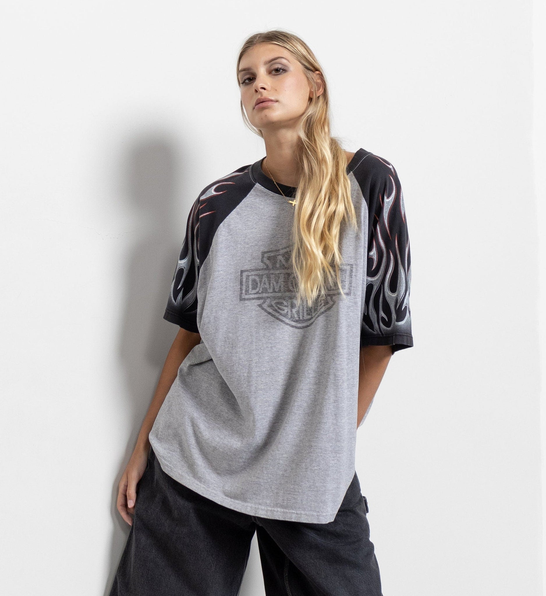 A person wearing a gray vintage t-shirt with black sleeves featuring a flame design and a restaurant logo on the front, paired with black shorts.