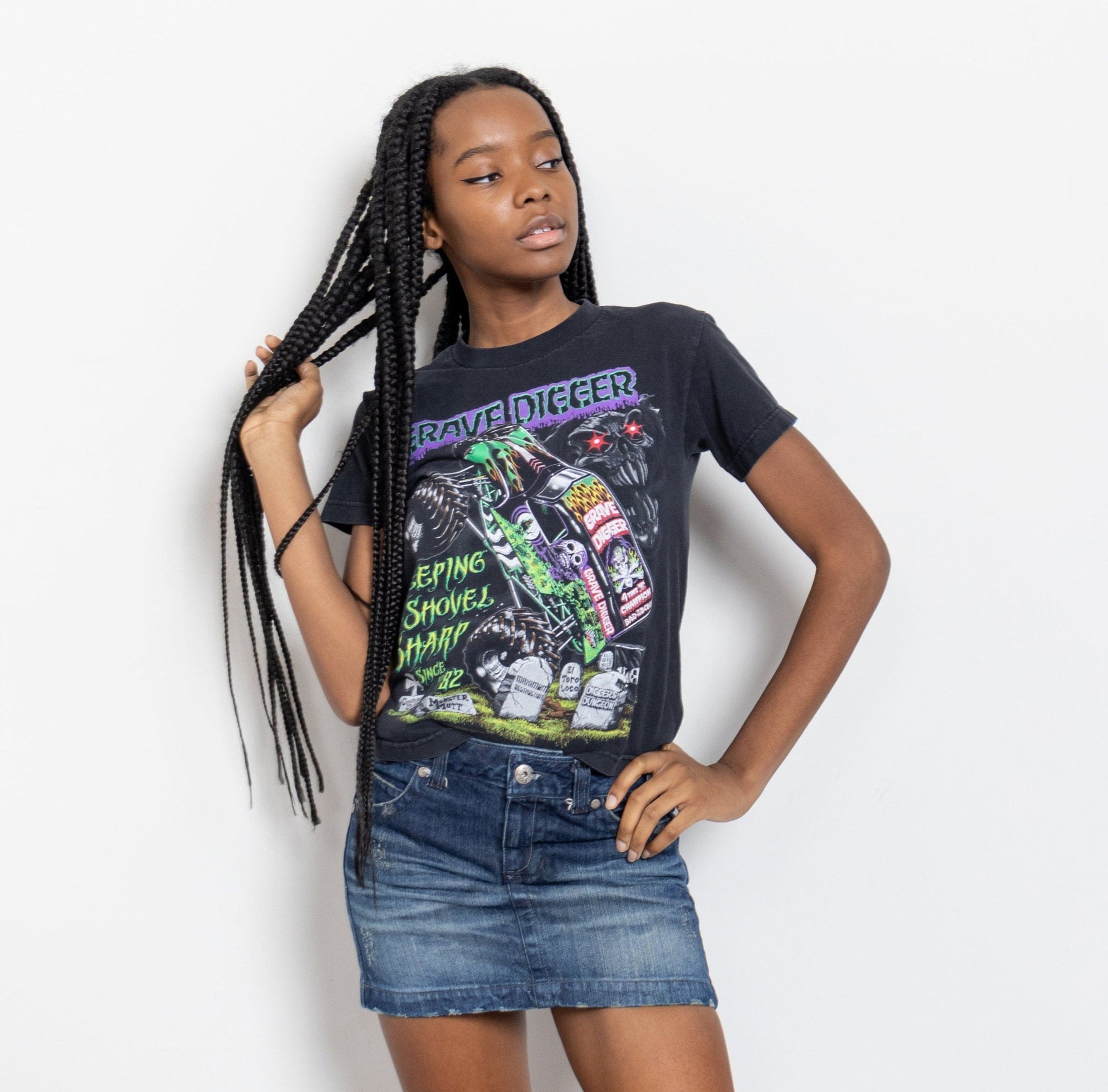 A person wearing a faded black t-shirt with a 'Grave Digger' print, featuring a cemetery scene with tombstones, skeletons, a demon rider, and a hot rod.