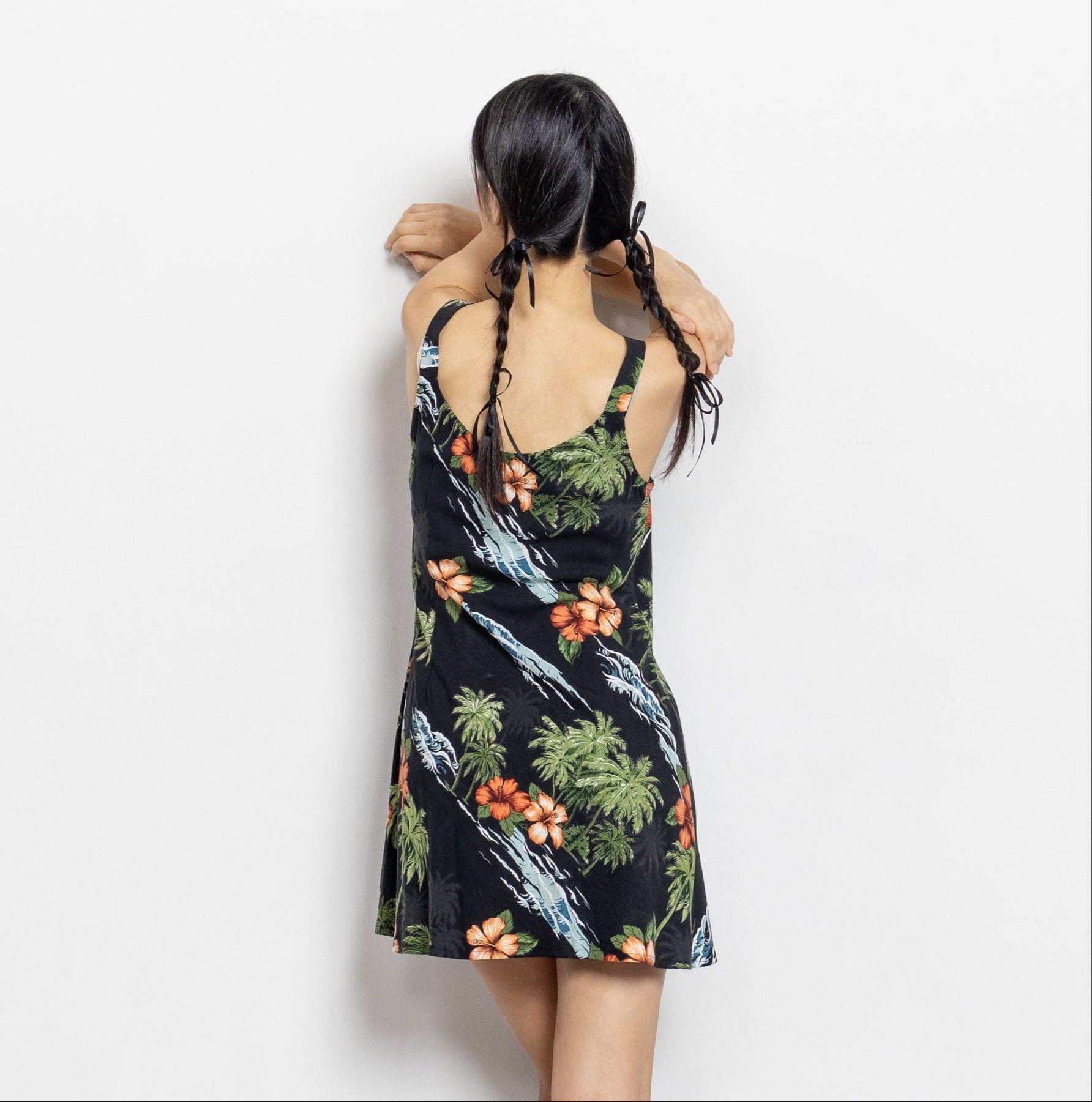 A sleeveless mini sundress with a tropical plants pattern in black, green, and rust colors, viewed from the back. Cute.