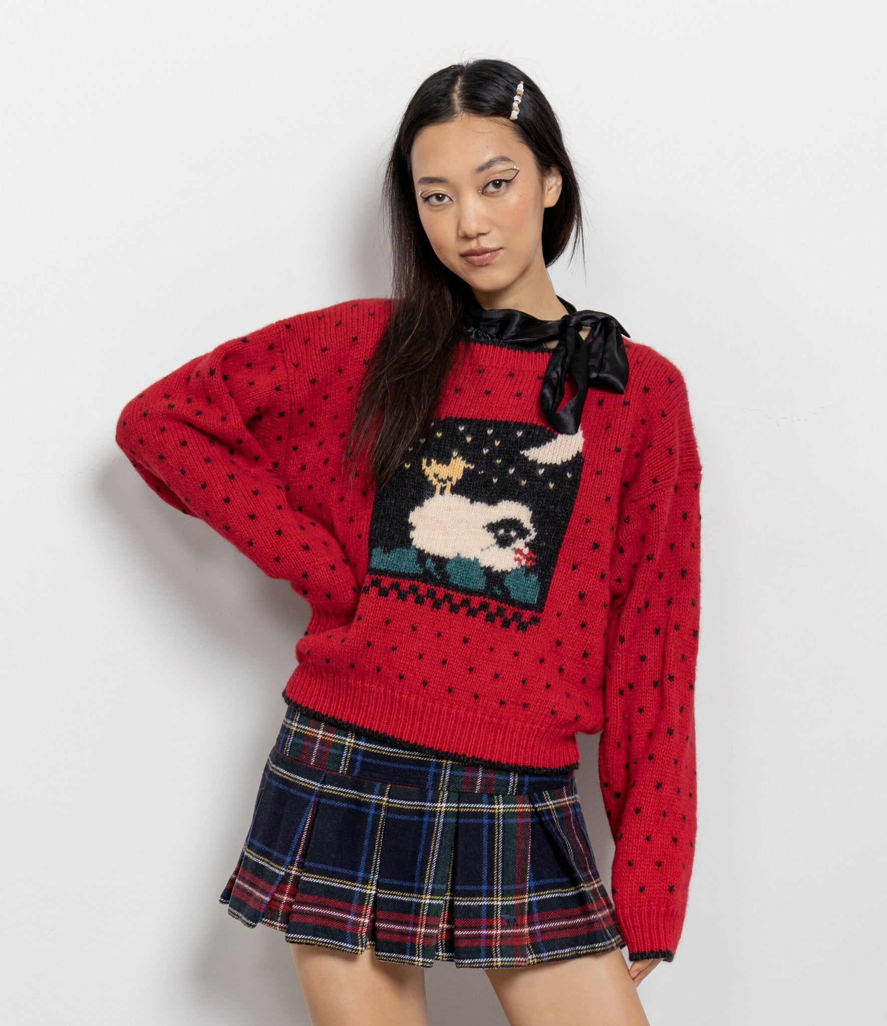 Person wearing a red sweater with a graphic design and a plaid skirt on a white background