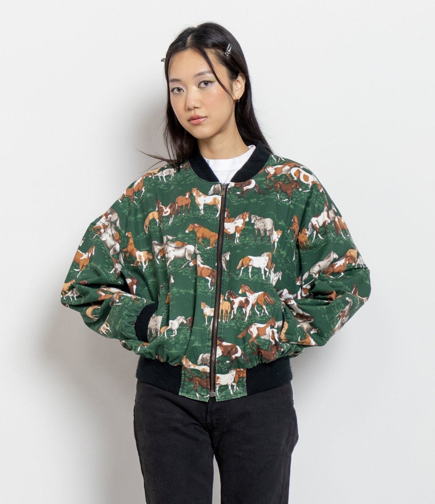 Person wearing a green bomber jacket with horse pattern on a white background