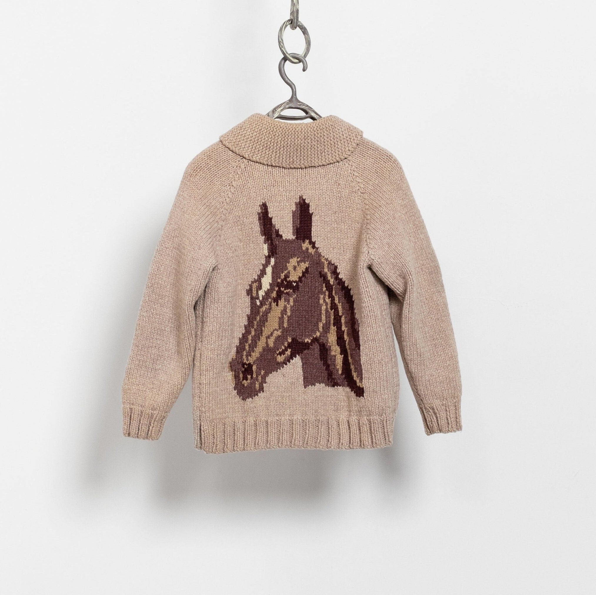 A beige handknit horse-patterned cardigan hanging against a white background.