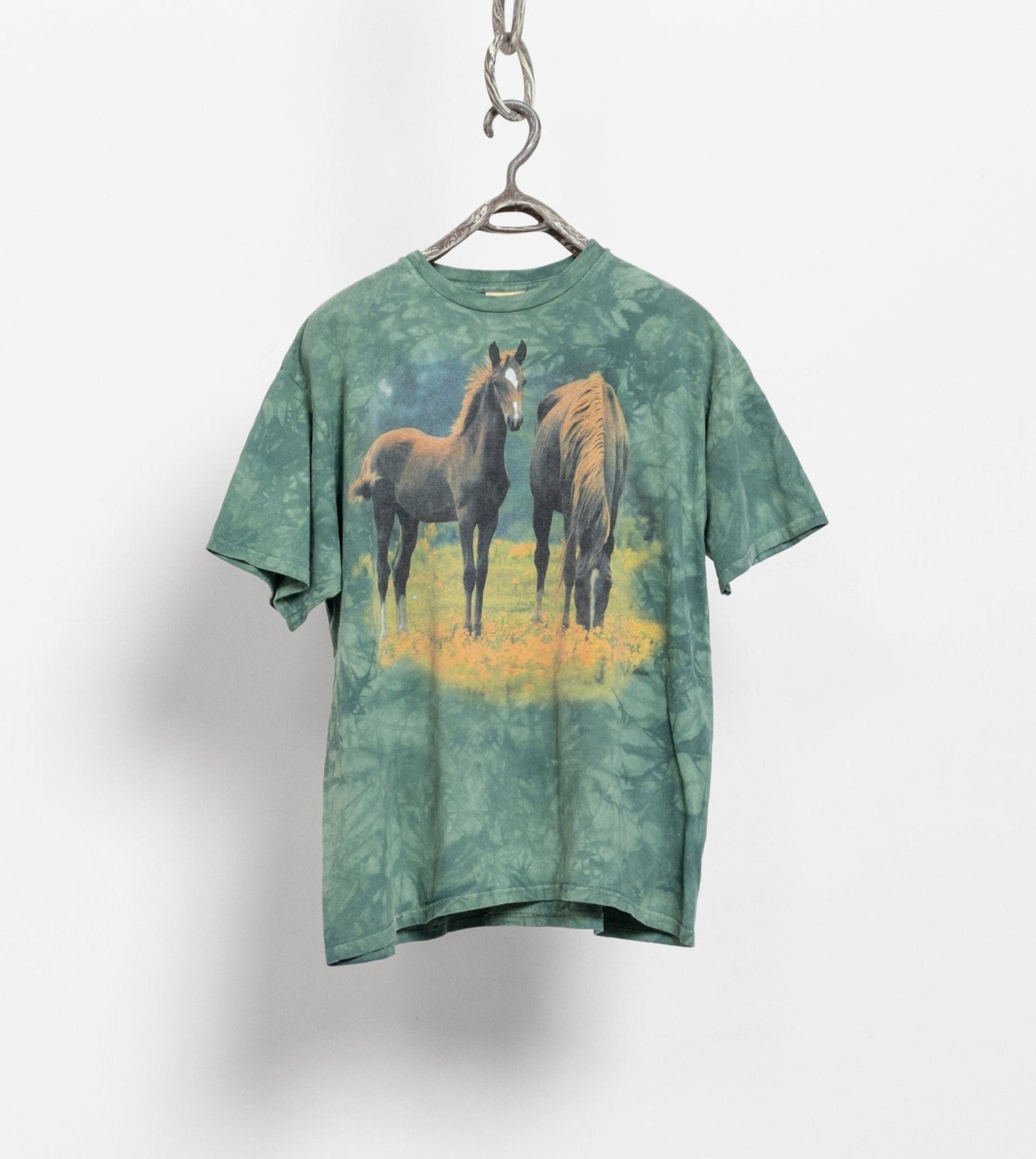 A green tie-dye graphic t-shirt with wild horse imagery, hanging on a display hook.