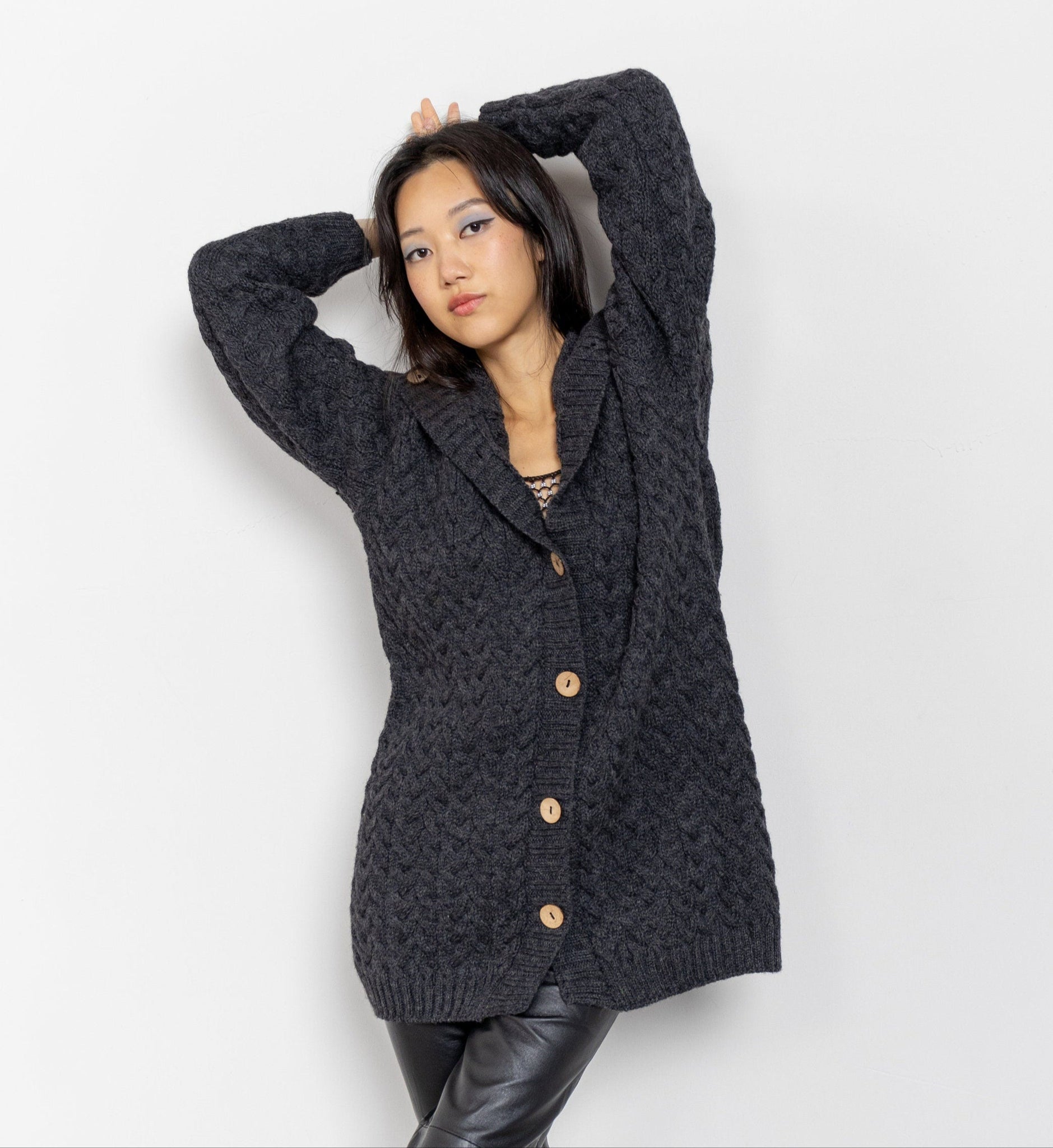 A woman posing with her hands raised wearing a dark heather grey button-up cardigan over a white top, paired with black pants.