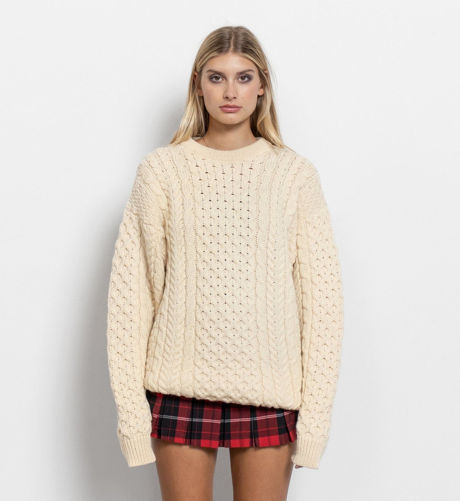 Woman wearing a cream sweater, plaid skirt, and black knee-high boots on a white background