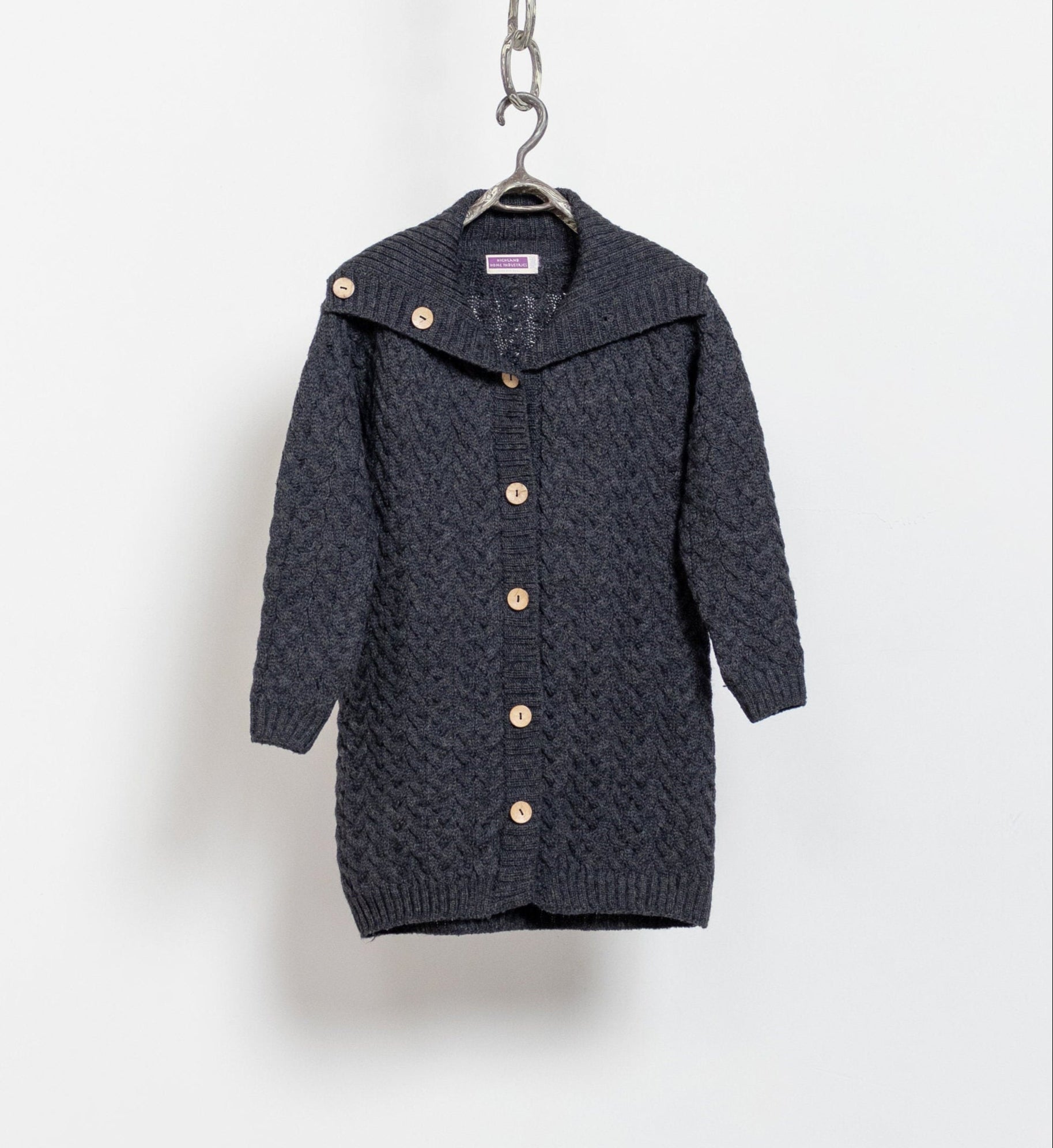 Dark gray knitted cardigan with gold buttons on a hanger against a white background