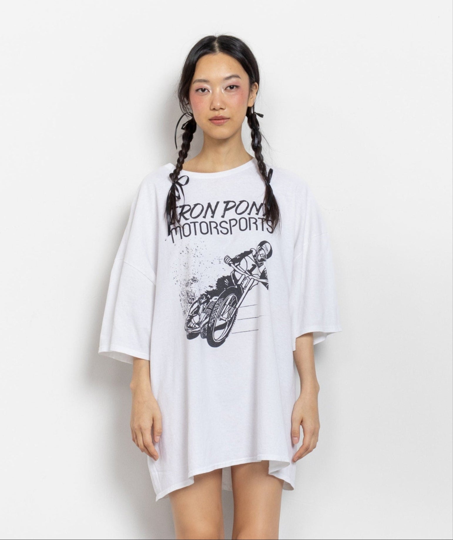A person wearing a white, oversized graphic t-shirt with 'Iron Pony Motorsports' and a cartoon motorcyclist on it.
