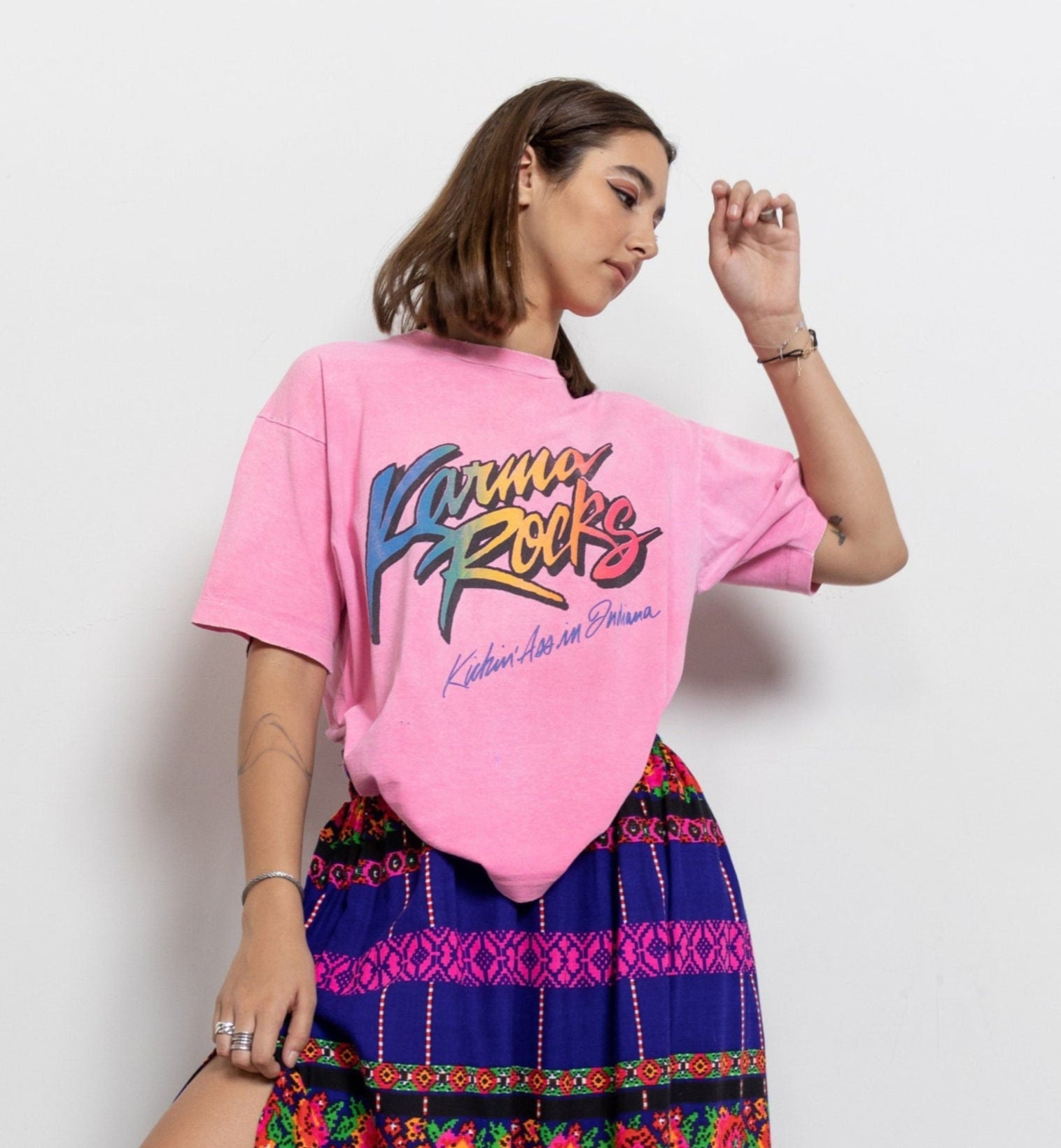 A person wearing a hot pink 'Karma Rocks' graphic t-shirt with multicolored graphics, standing against a plain background.