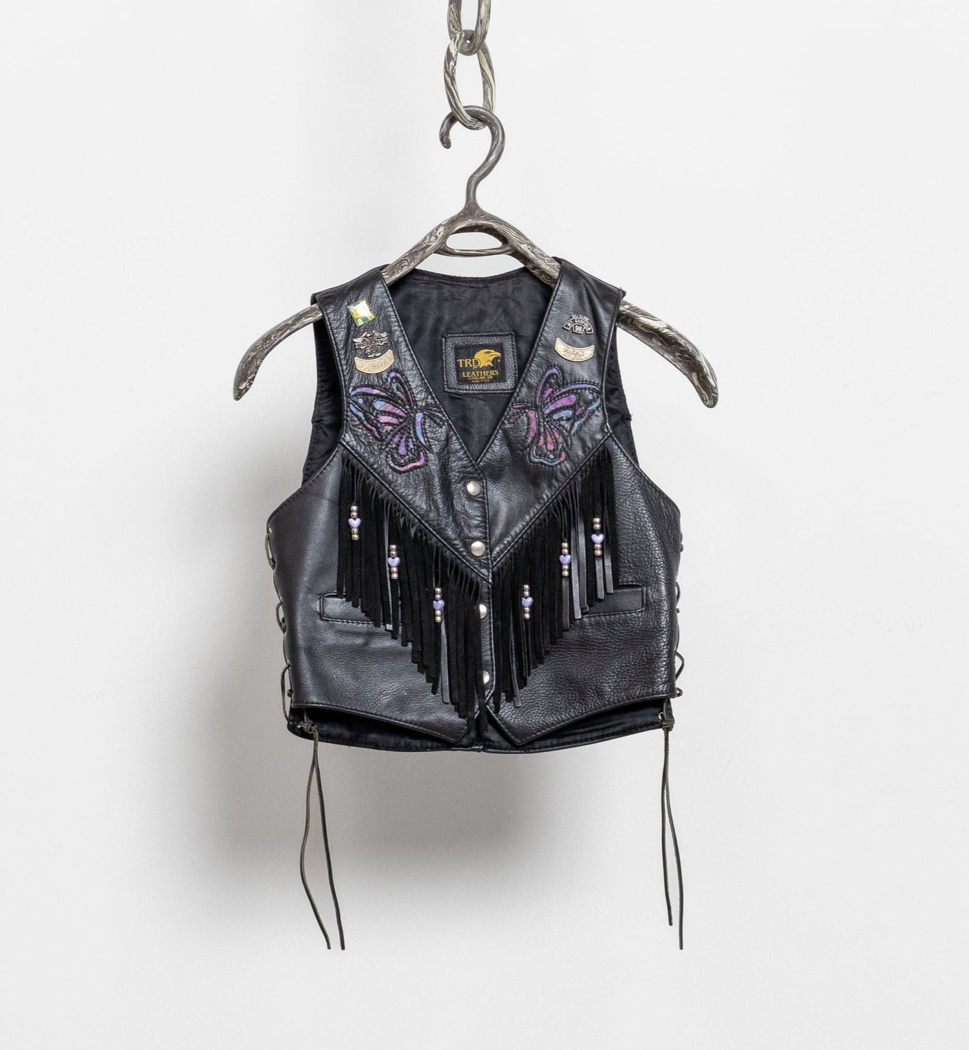 Black leather vest with fringe and embroidery on a hanger against a white background