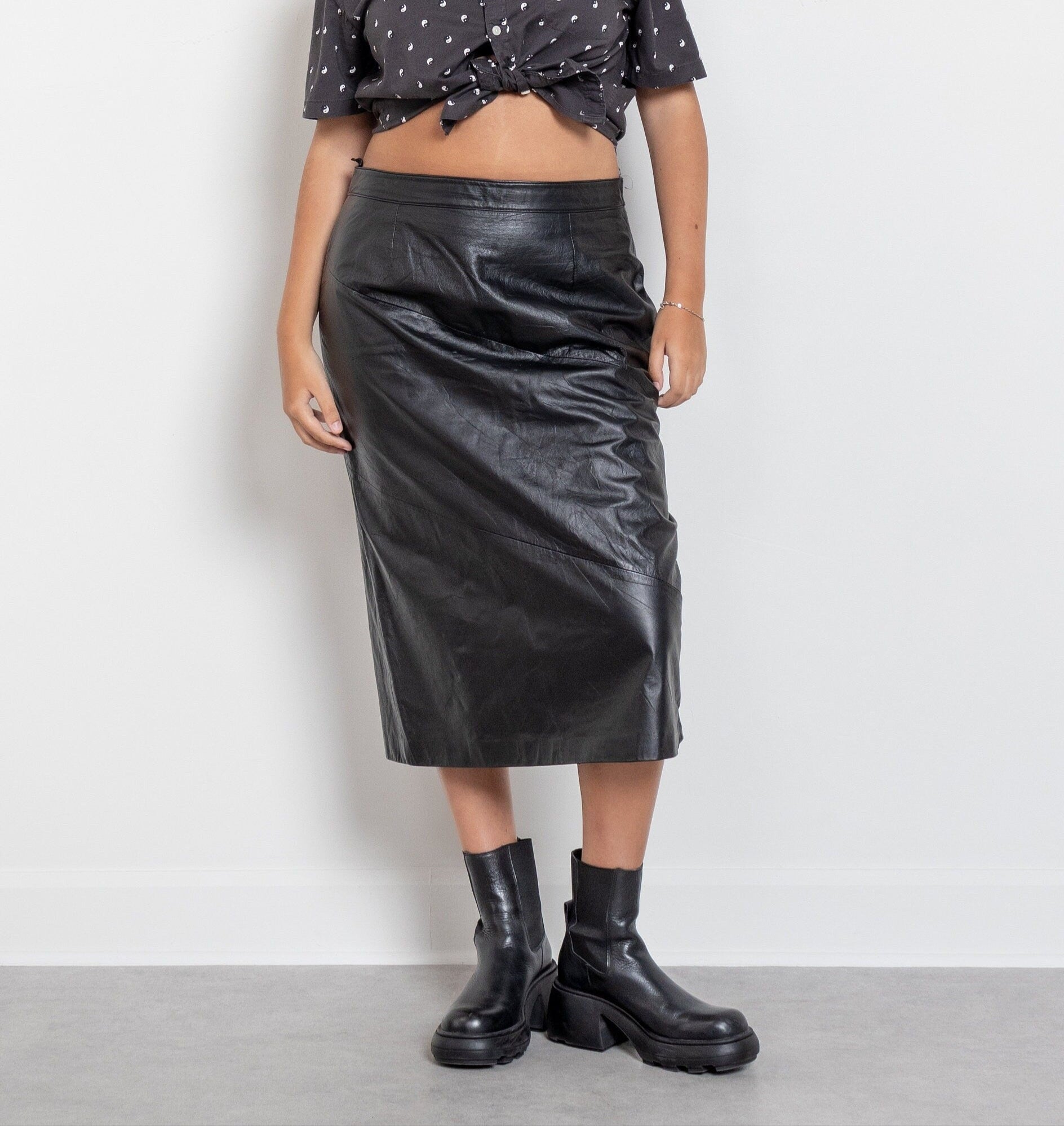Person wearing a black leather skirt and black boots on a plain background