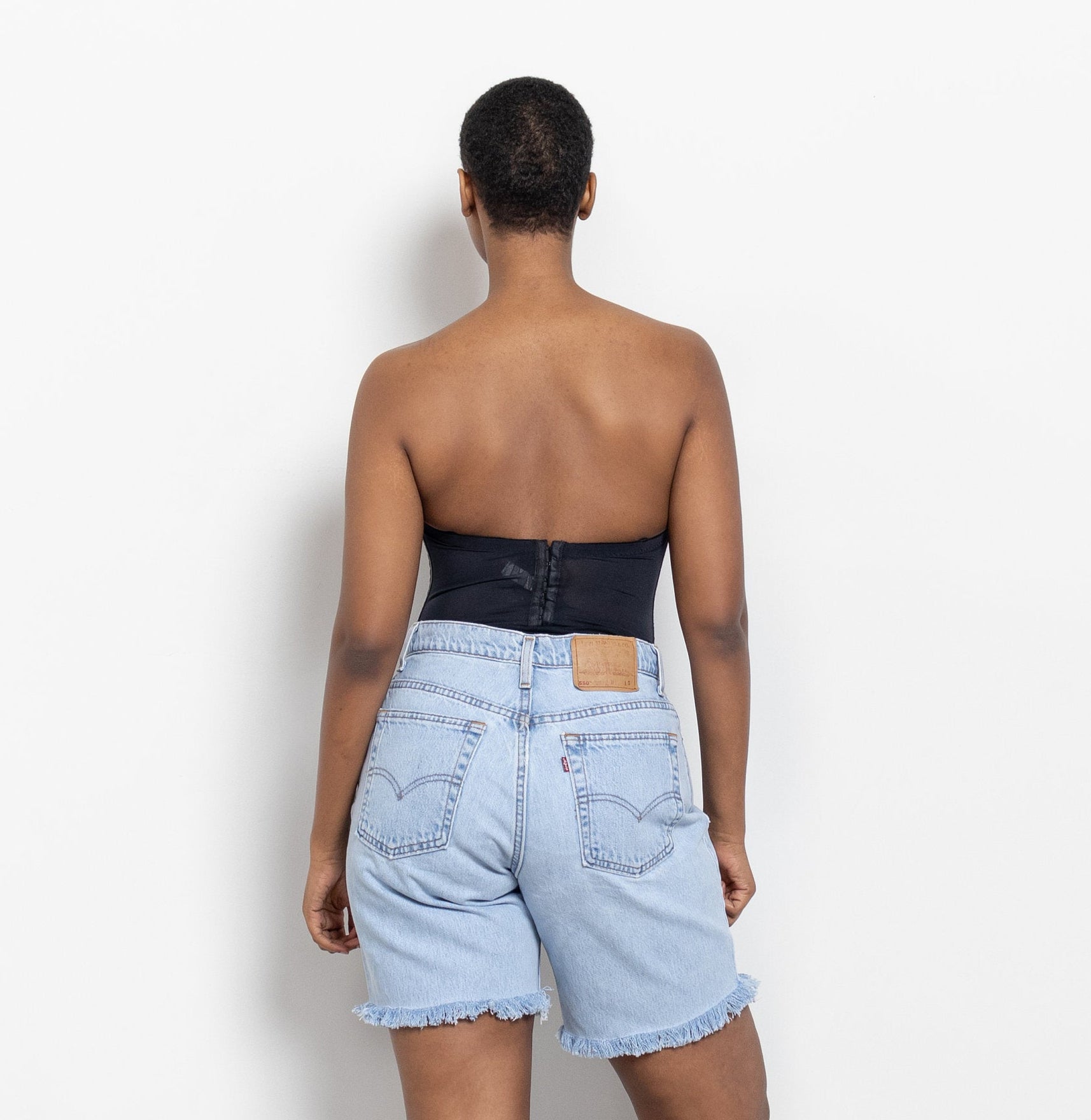 A person viewed from the back wearing a black strapless top and light wash denim shorts with a frayed hem.