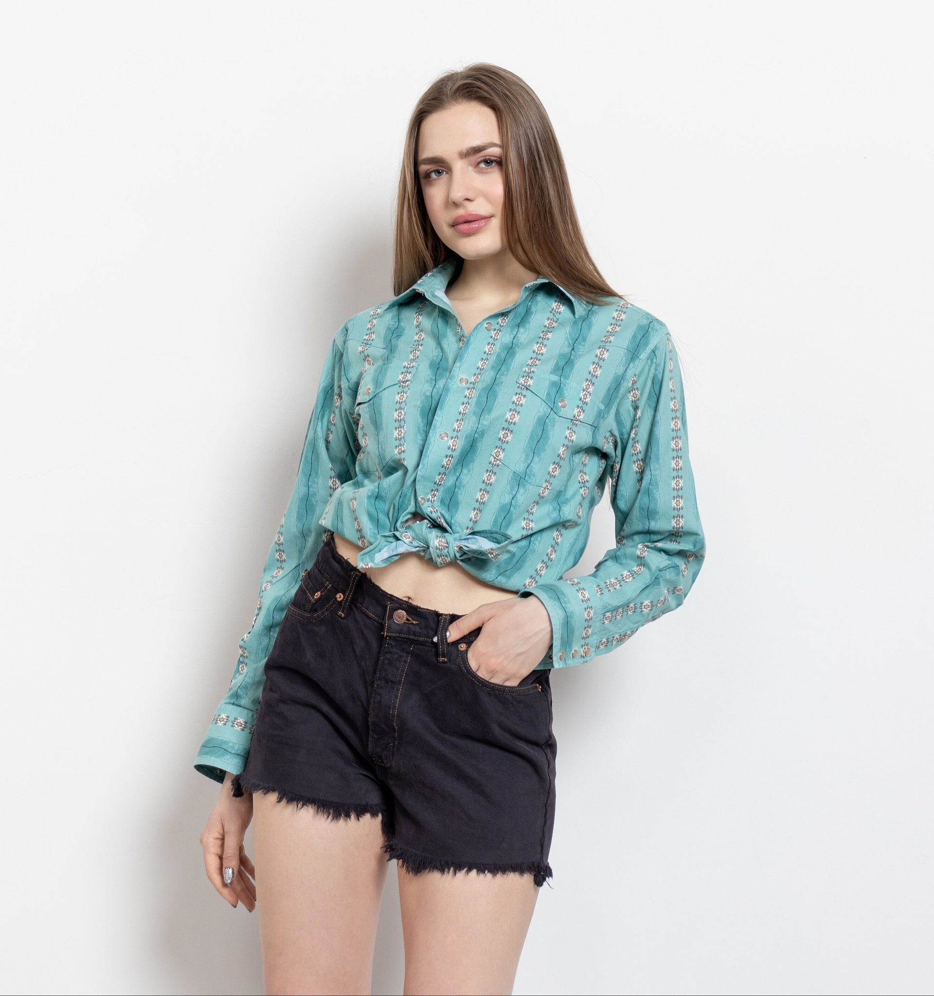 A person wearing a turquoise geometric patterned shirt and black cut-off denim shorts.