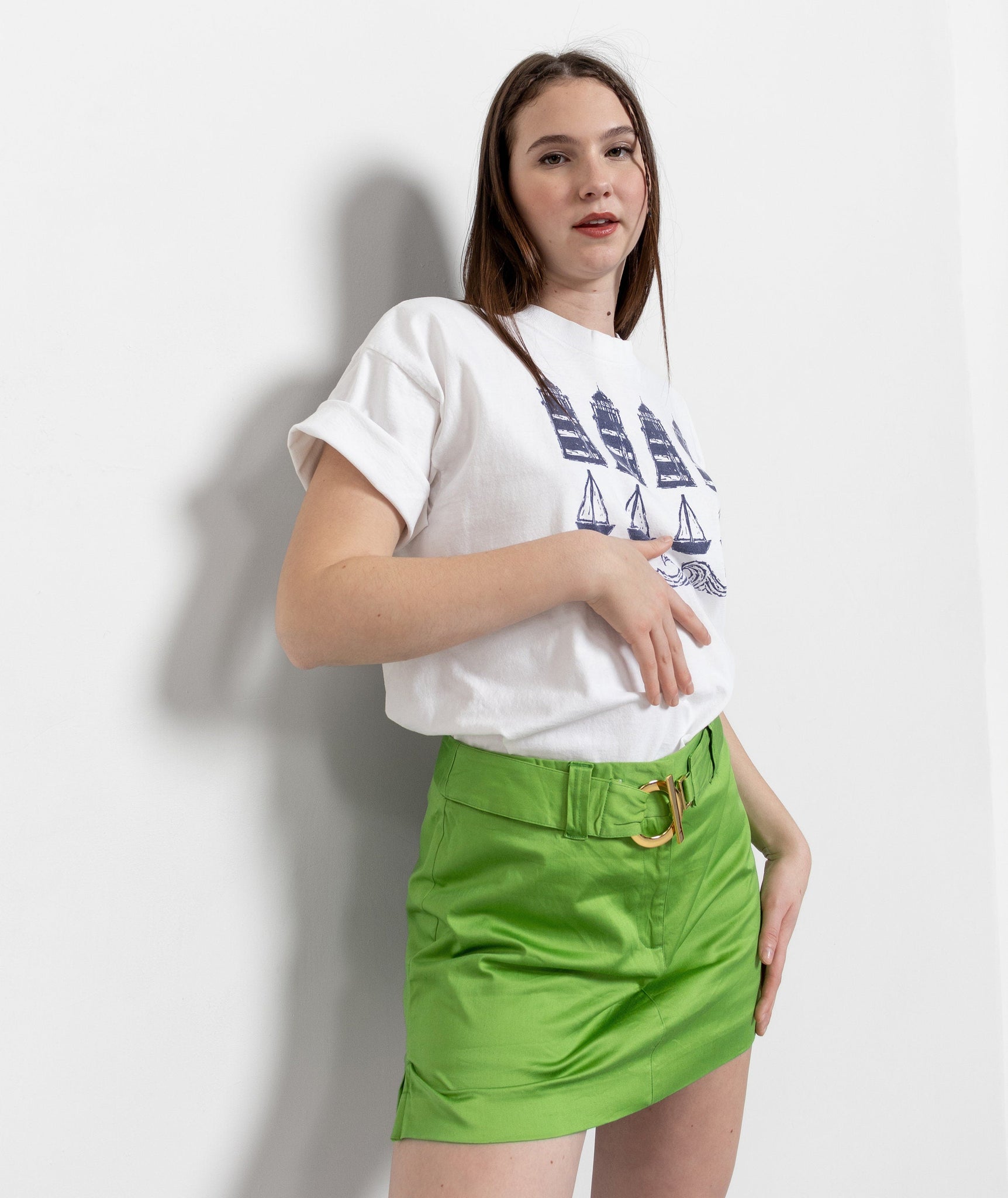 Woman wearing a white t-shirt with a graphic design and a green skirt on a plain background
