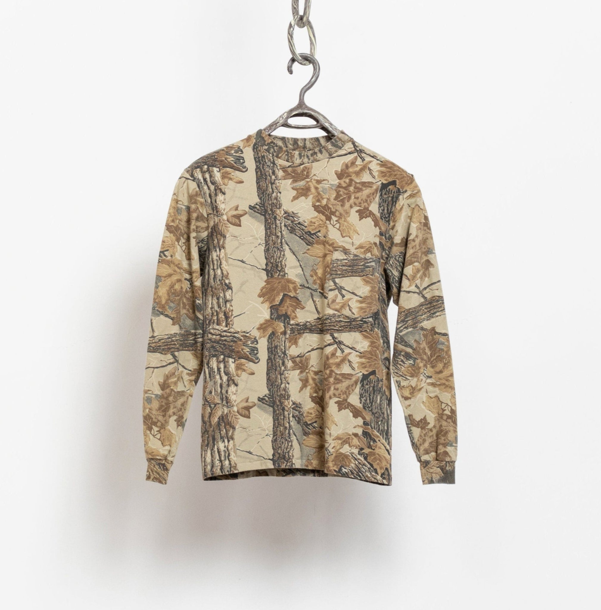 A long sleeve camouflage t-shirt with a leaf print, hanging on a hanger against a white background.