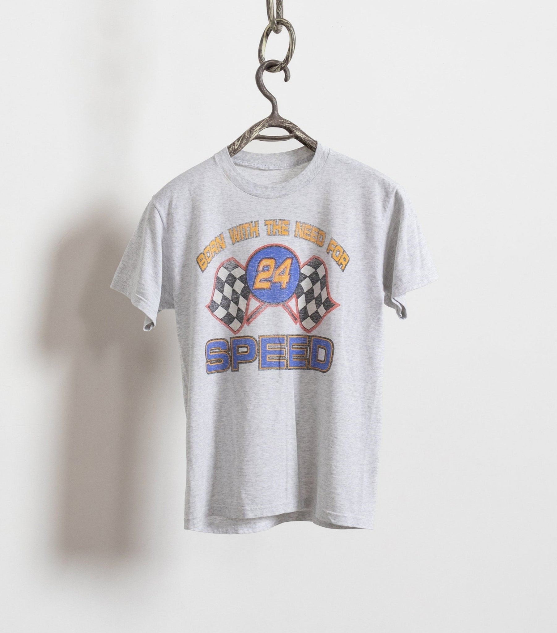 A vintage gray t-shirt with a colorful 'Need For Speed' racing graphic hanging on a hanger against a white background.