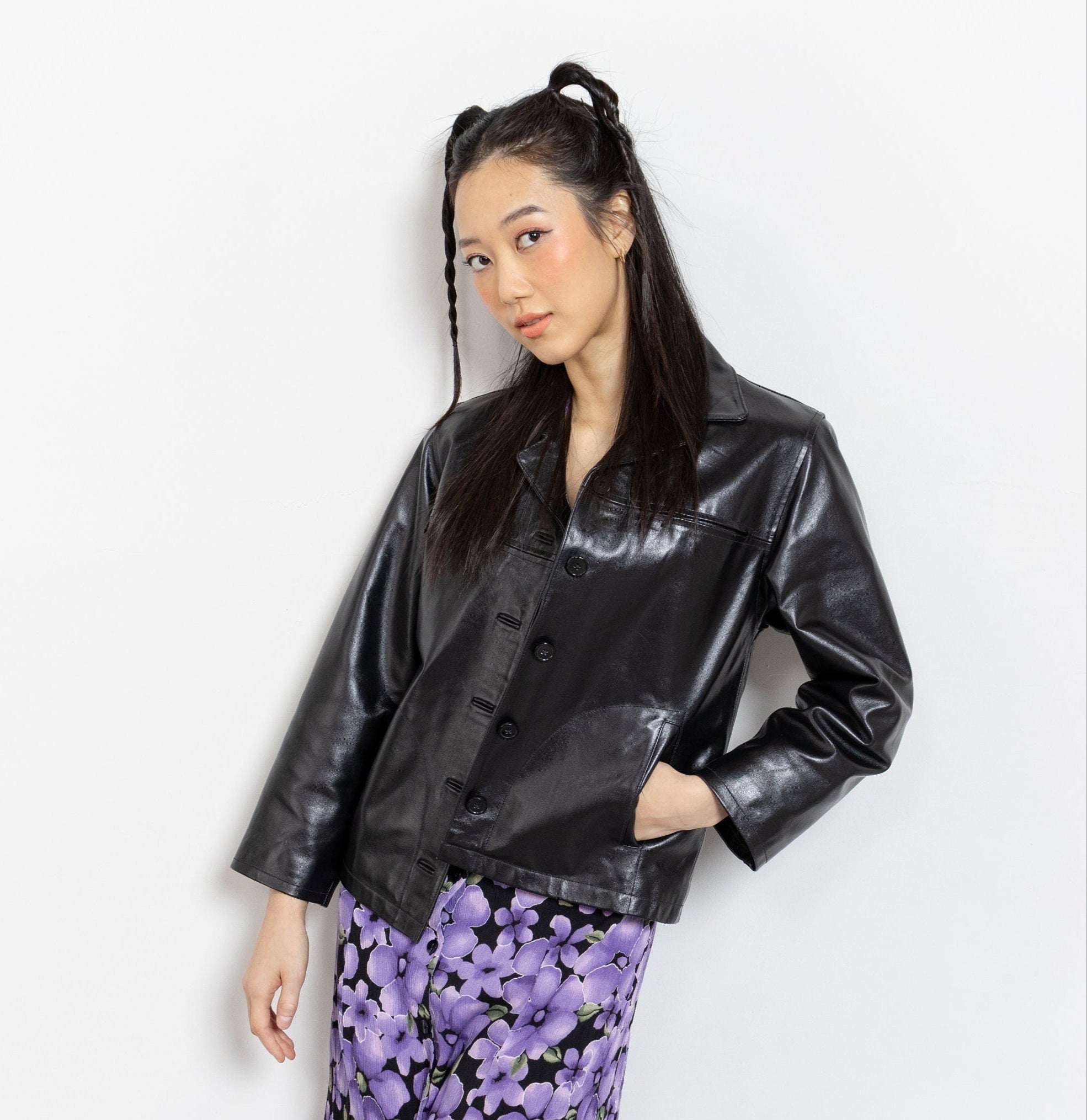 Woman wearing a black leather jacket and purple floral pants on a white background