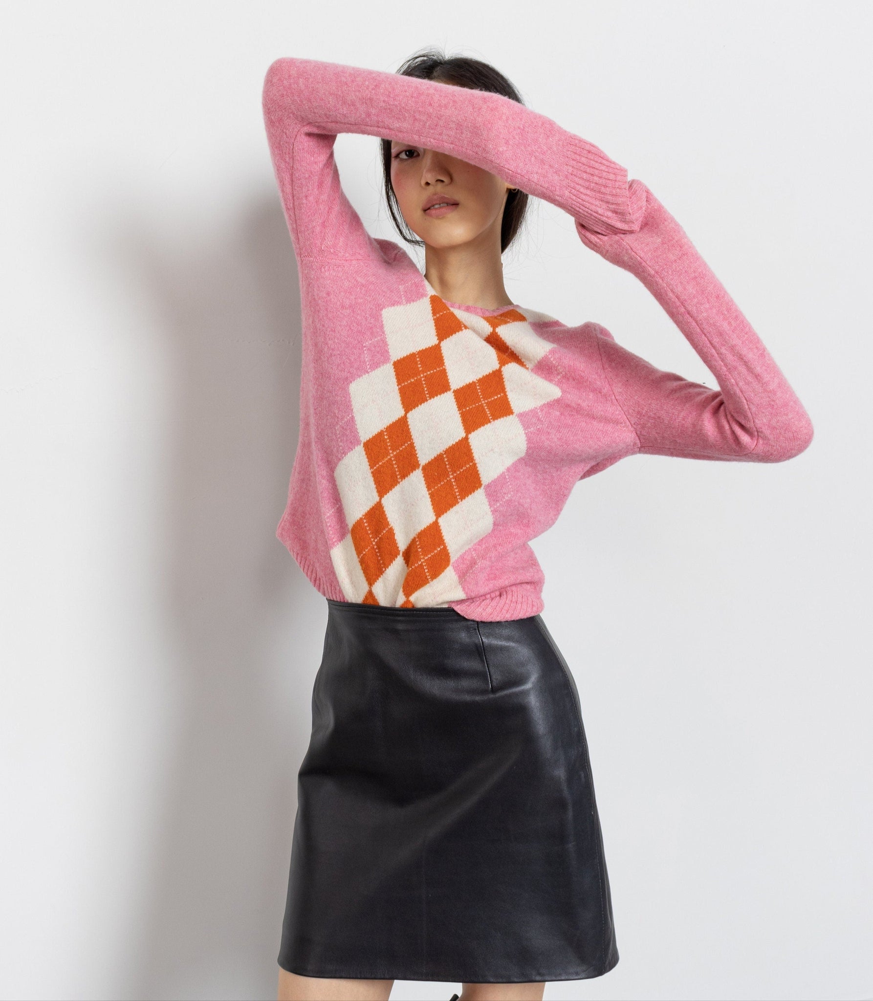 Person wearing a pink sweater with a diamond pattern and a black leather skirt on a white background