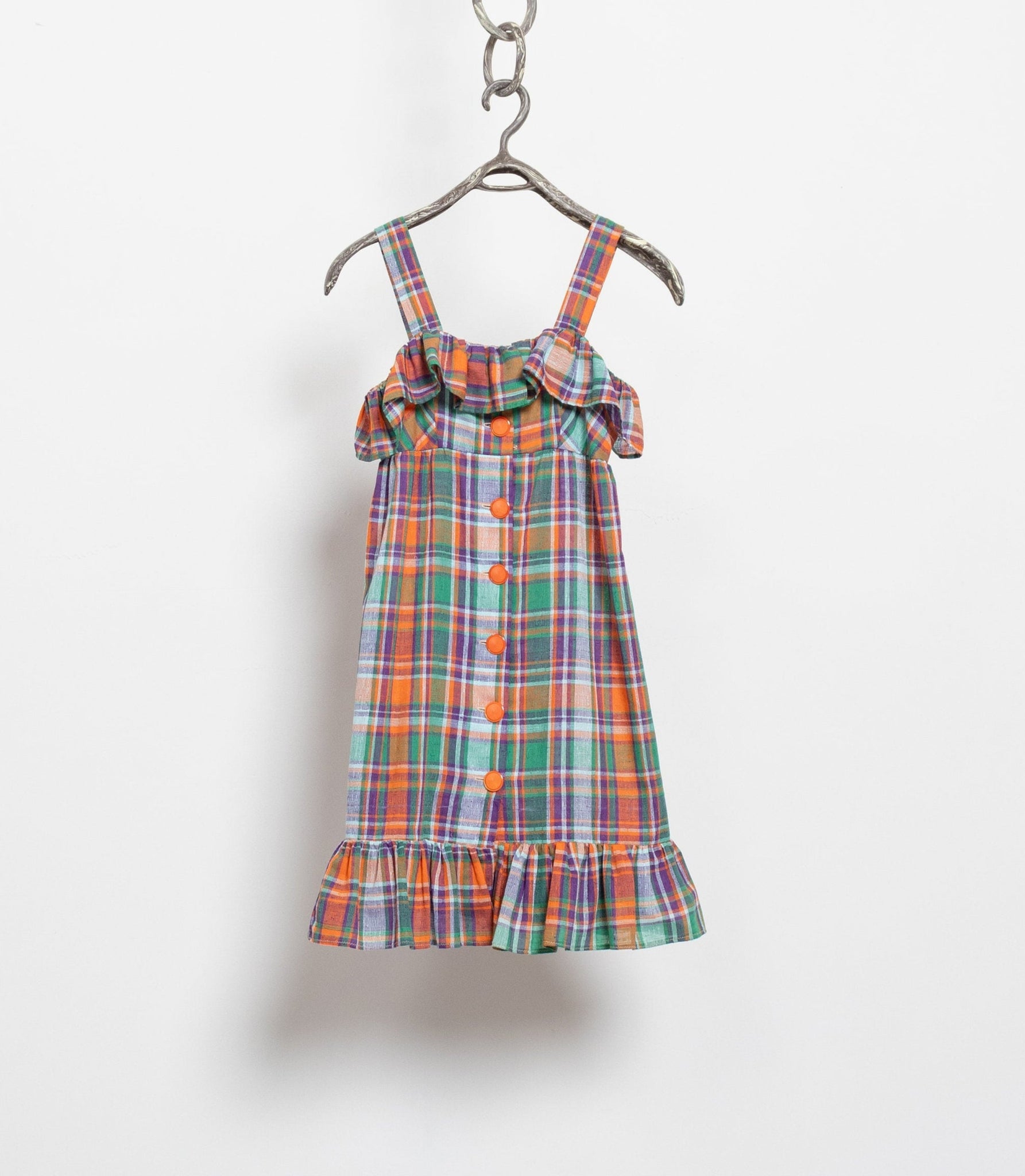 A vintage plaid cotton midi dress with wide shoulder straps, orange buttons, and ruffles at the hem and top of the bodice, hanging on a hanger against a white background.