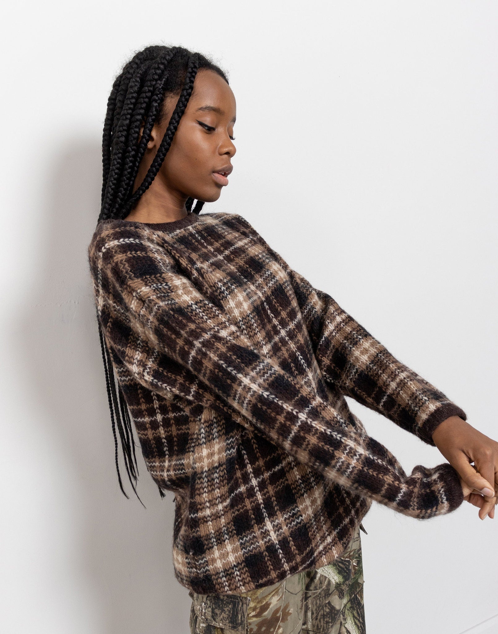 Person wearing a plaid sweater and camouflage pants against a white background