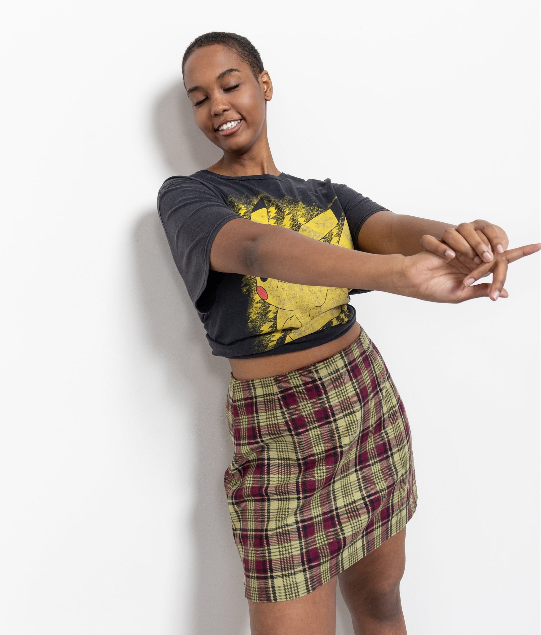 Woman wearing a black crop top with a graphic design and a plaid skirt on a white background